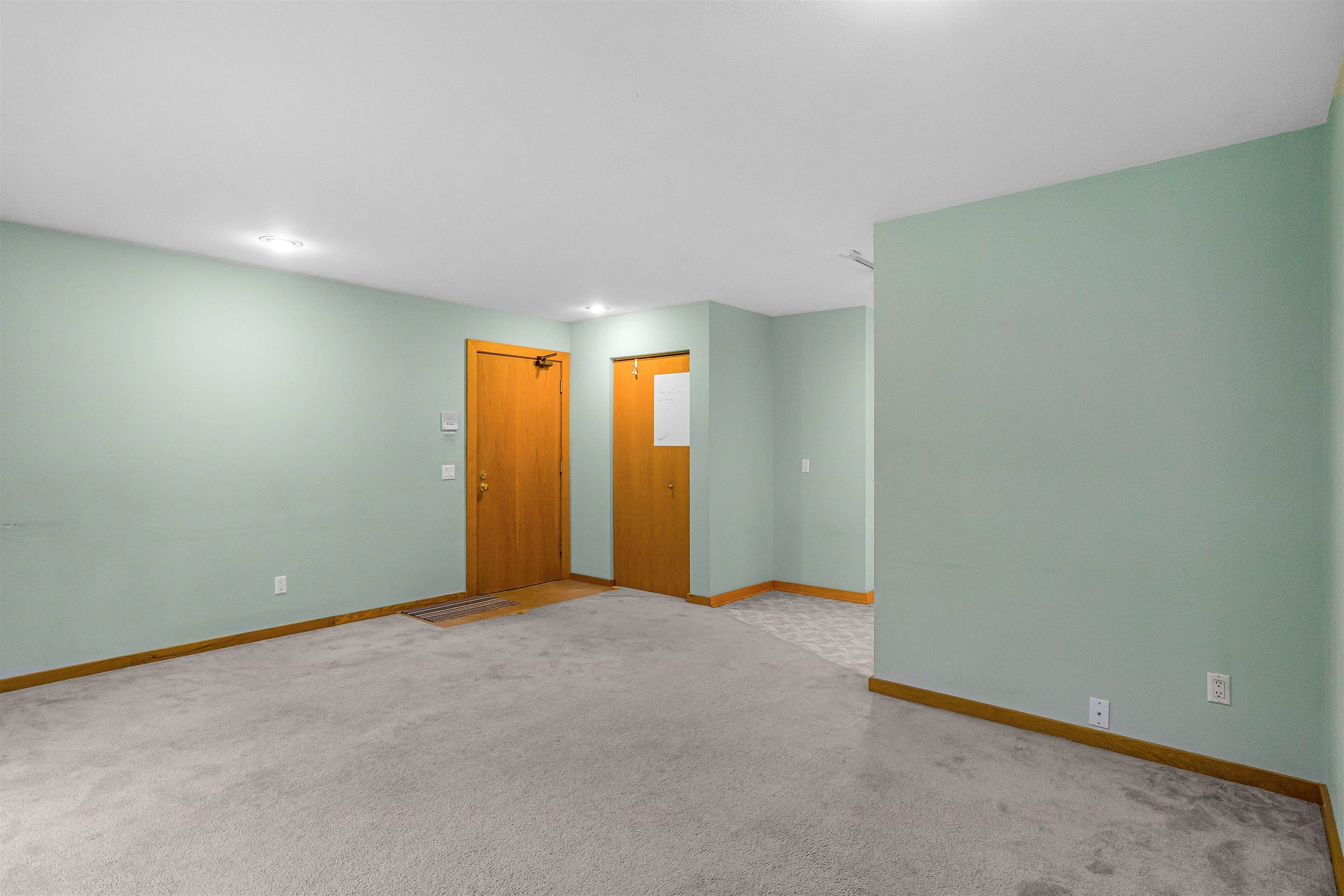 Empty carpeted room with pale green walls, wood trim, and two wooden doors.