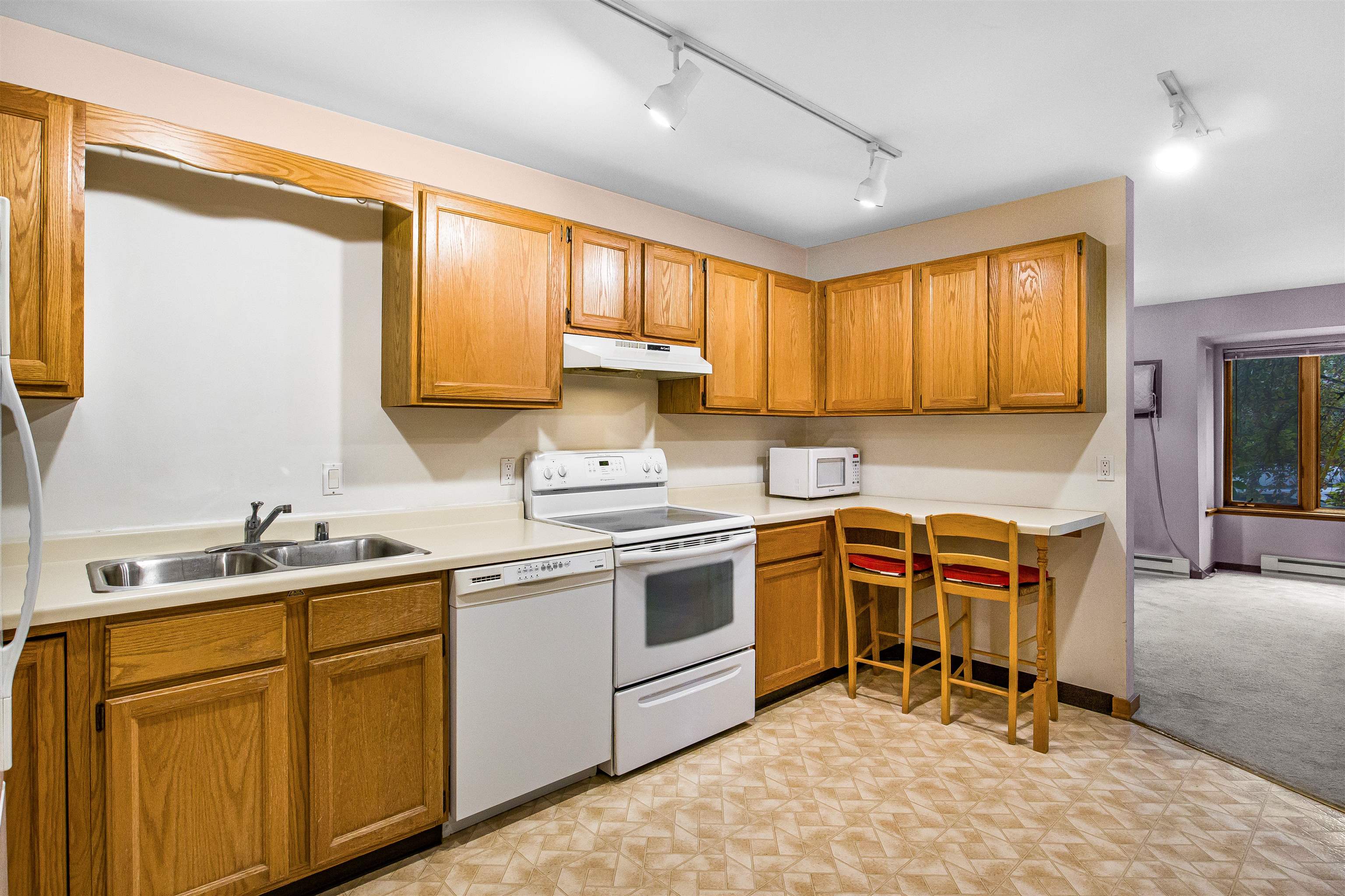 Kitchen with honey-colored cabinets, white appliances, a double sink, and a counter with two chairs.