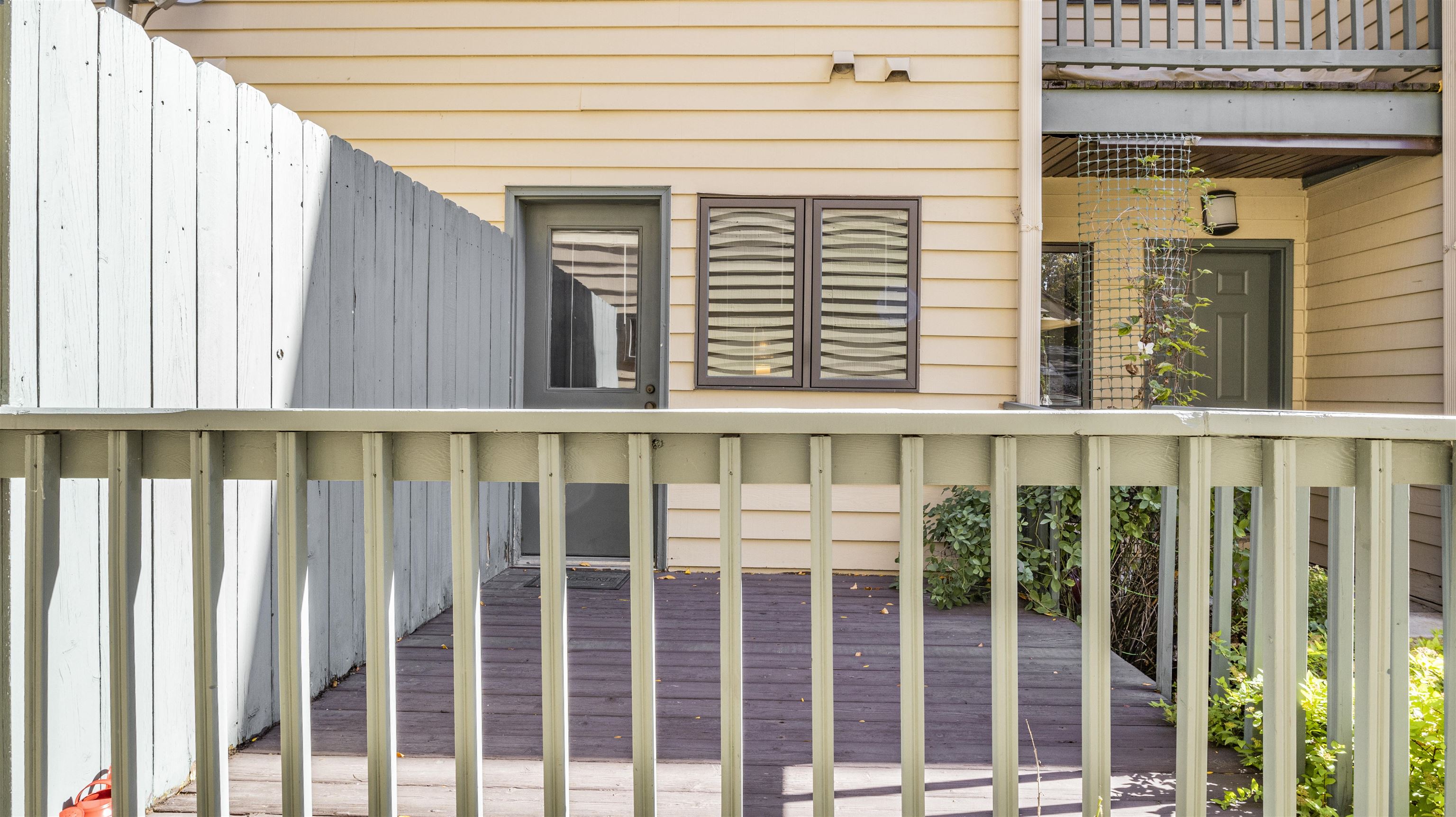 Wooden deck and entry with a pale railing, white privacy fence, and beige siding.