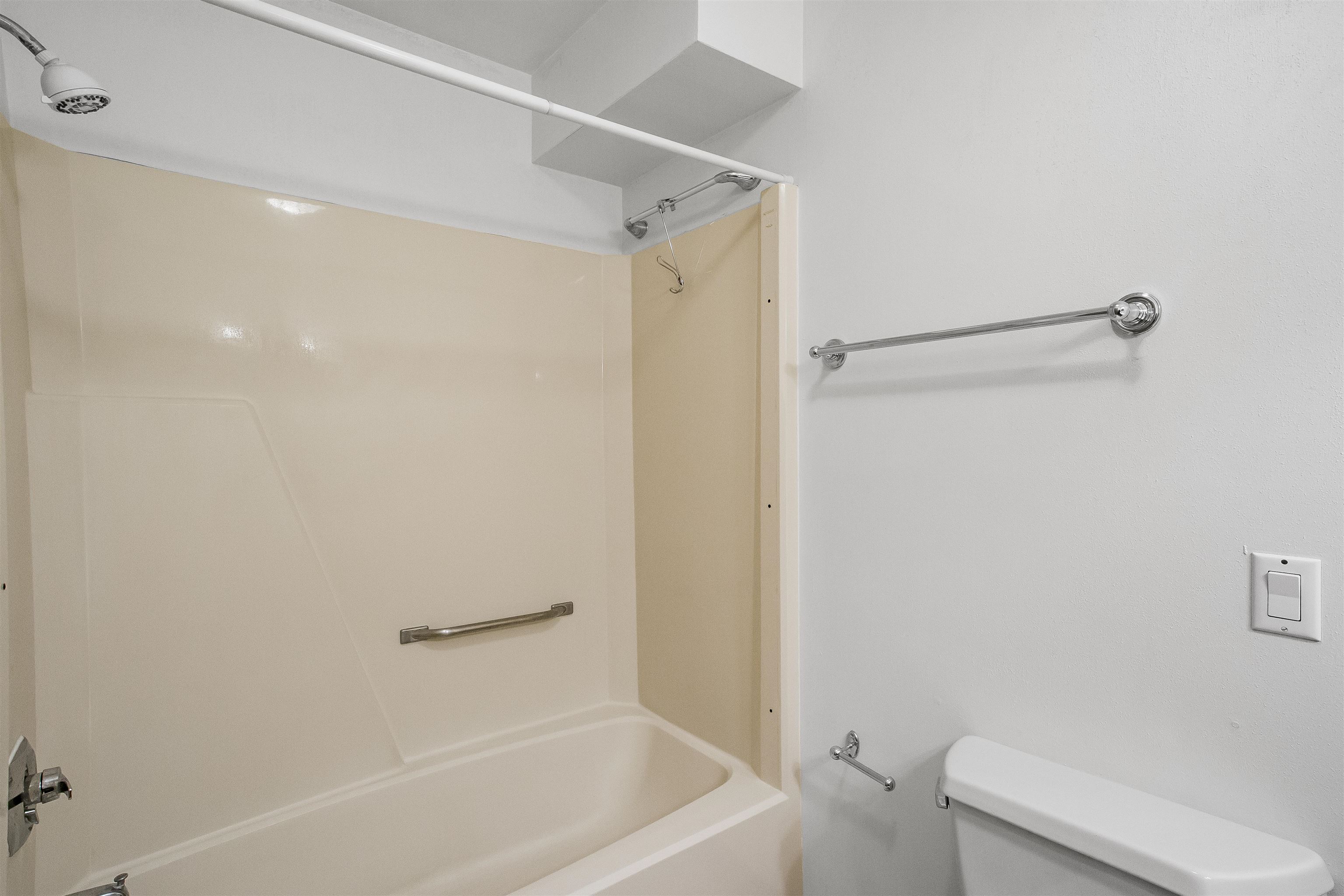 Bathroom with a beige tub and shower surround, chrome grab bars, and part of a white toilet.
