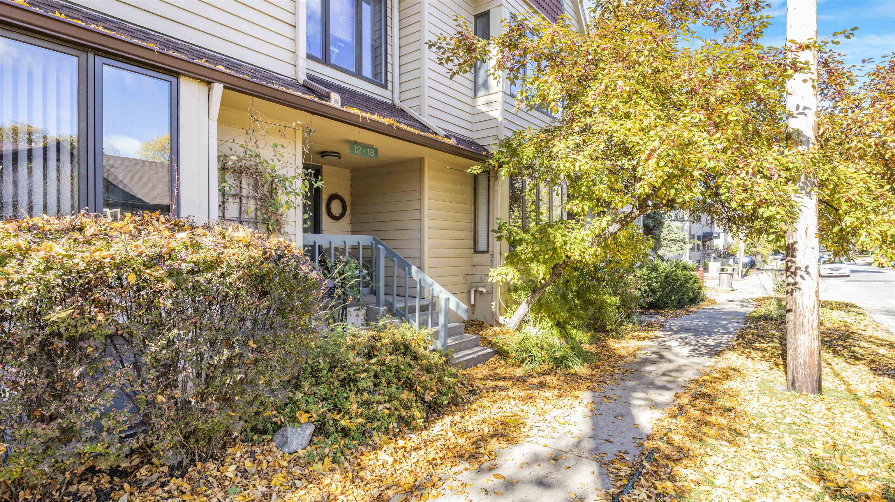 Residential building entrance with blue-gray steps, autumn trees, and fallen leaves along the sidewalk.