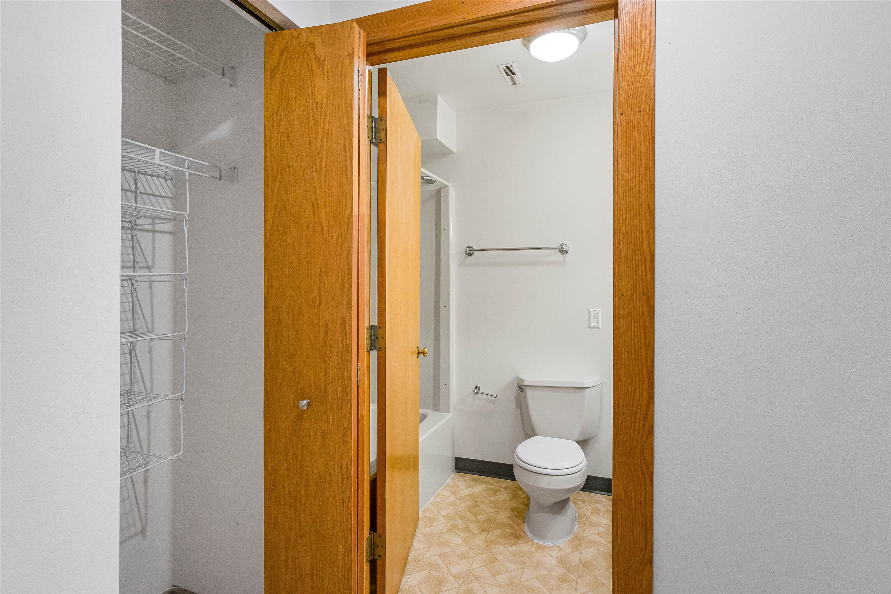 Bathroom with a toilet, grab bars, bathtub, and wire shelving beside the open doorway.