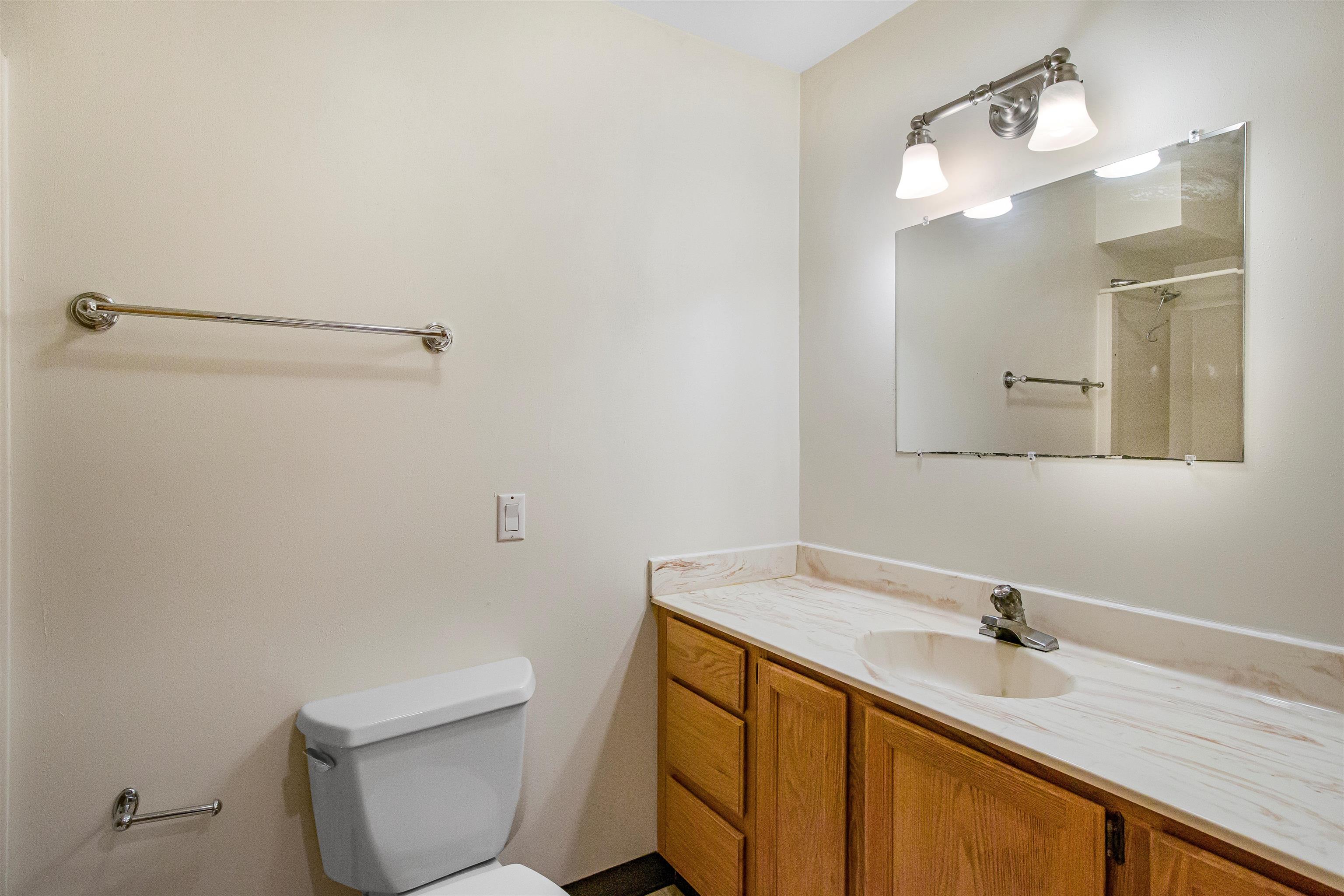 Bathroom with oak vanity, marble-look countertop, large mirror, and toilet.