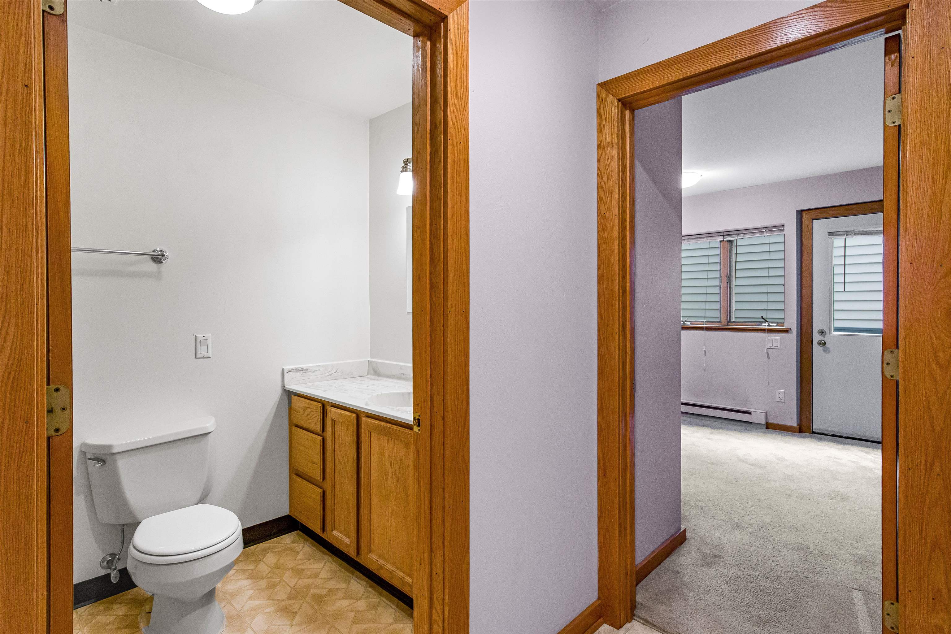 Bathroom with wood vanity and trim, viewed through doorways into an adjoining carpeted room.