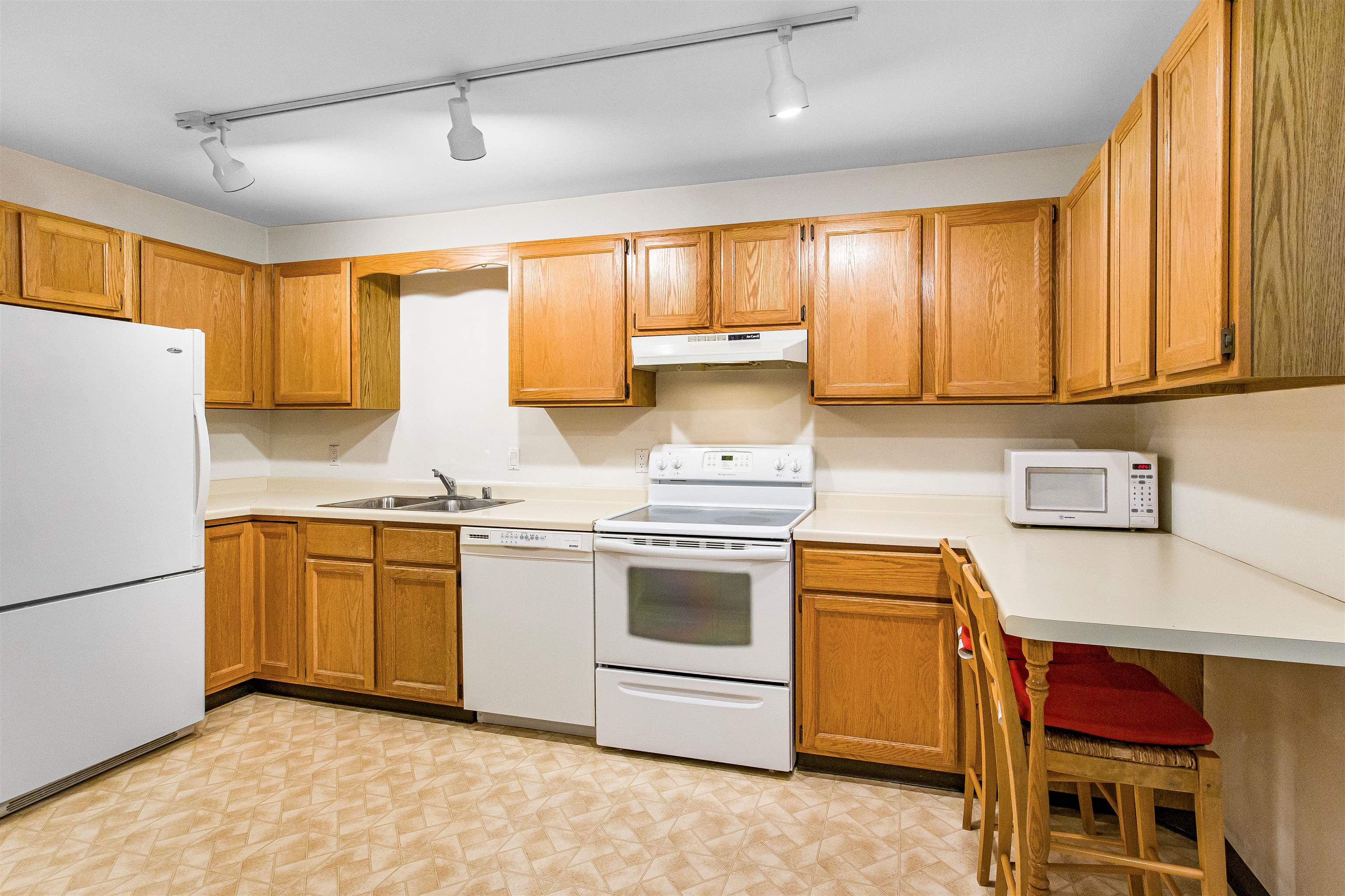 Kitchen with honey-colored cabinets, white appliances, and a breakfast counter with chairs.