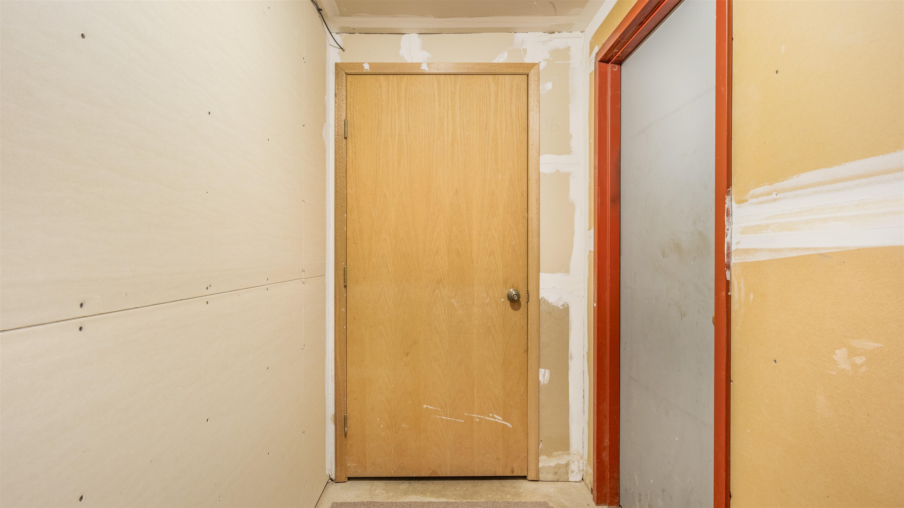 Unfinished hallway with a wooden door and red-framed opening.