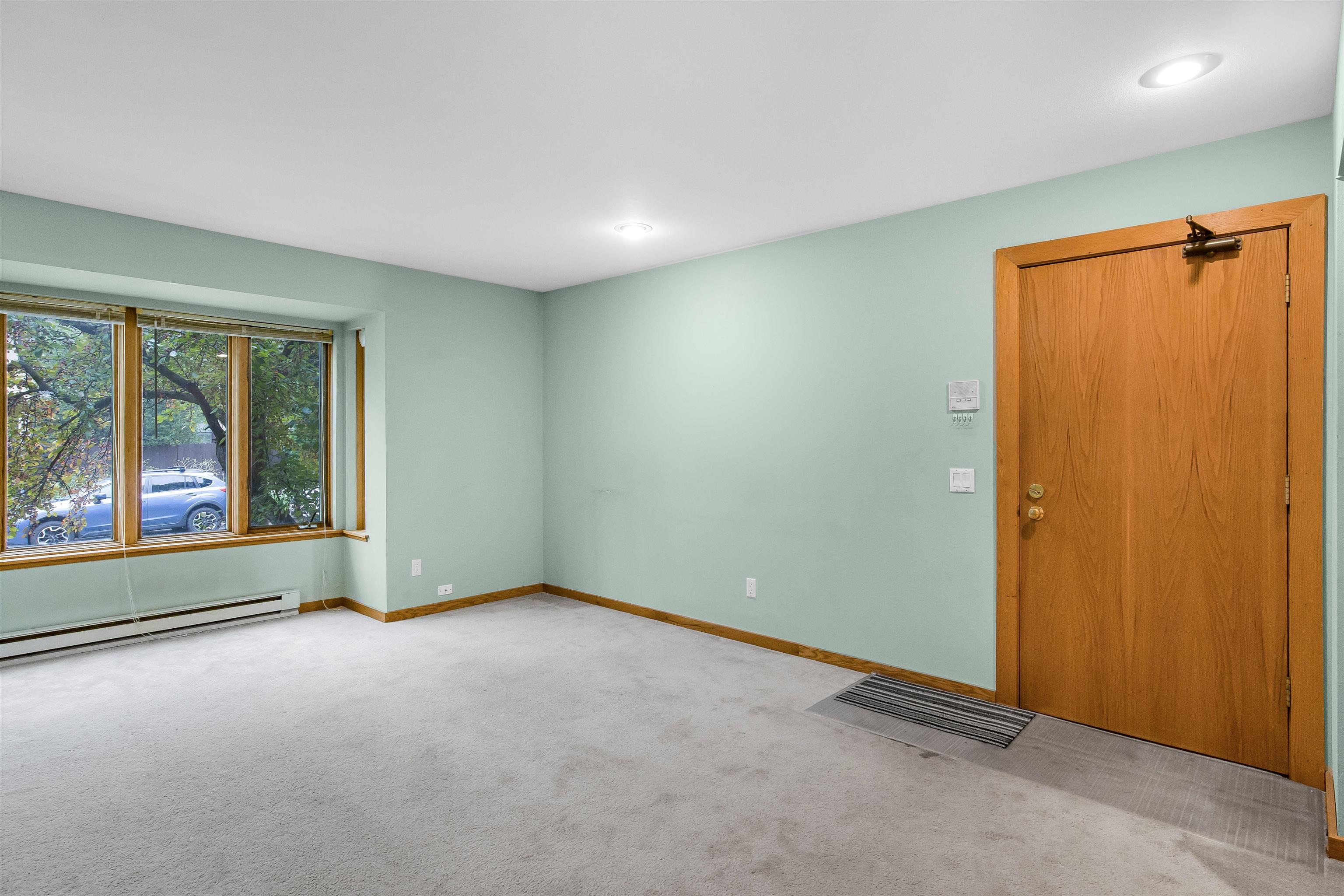 Empty room with pale green walls, carpet, a large window, and a wooden entrance door.