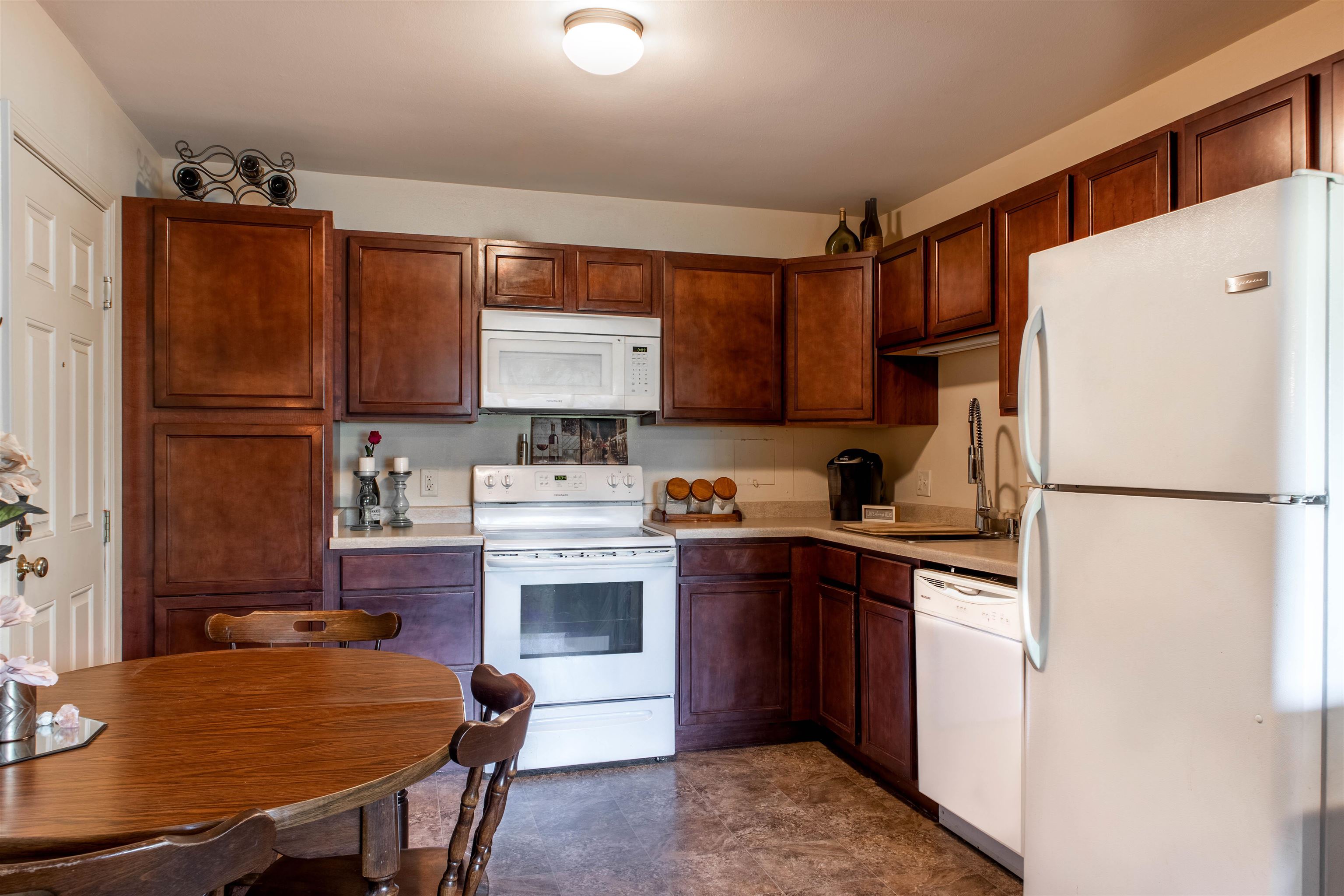 Kitchen with dark wood cabinets, white appliances, and a round wooden dining table.