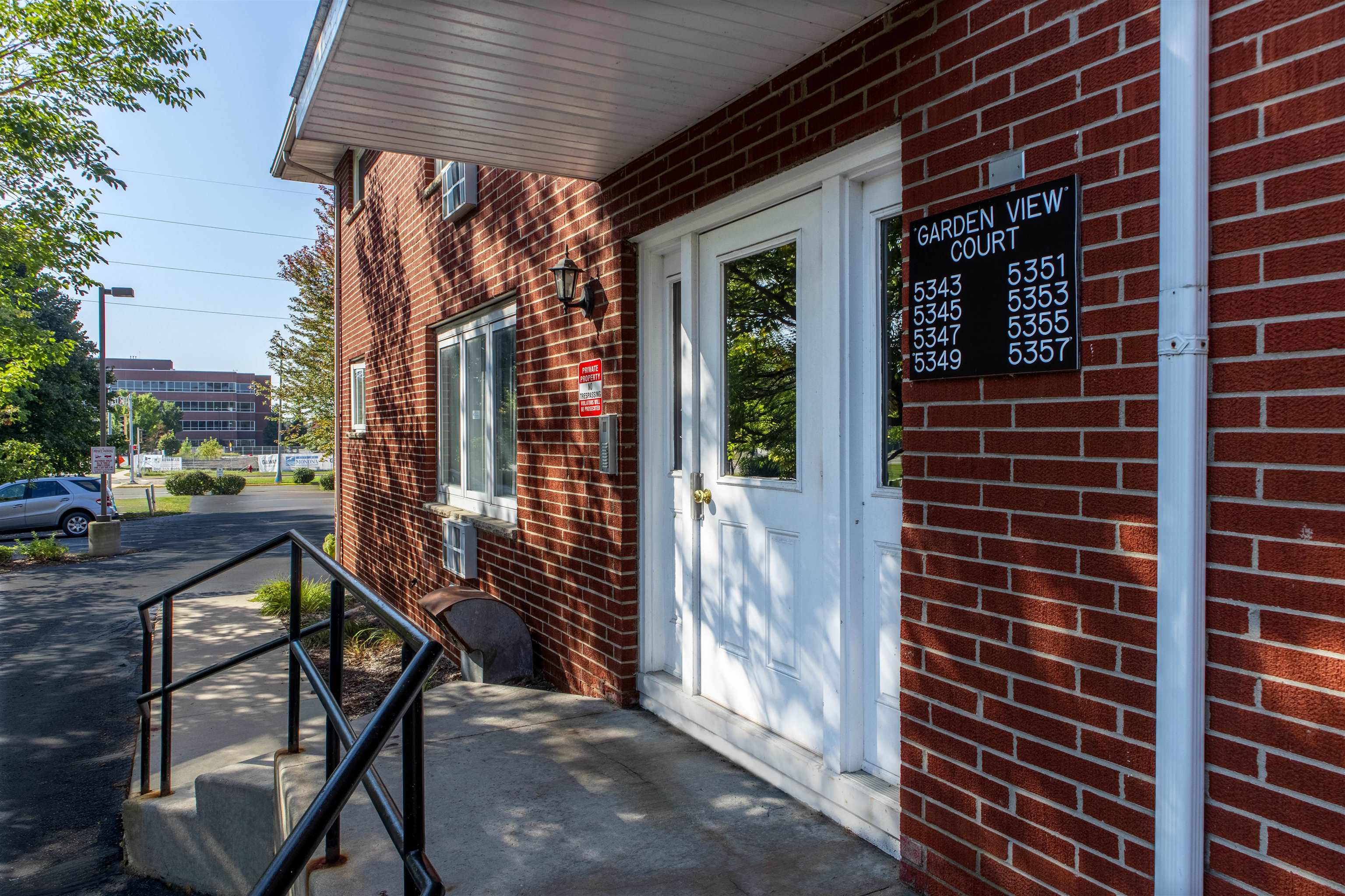 Red brick building entrance with white doors, black walkway railings, and a Garden View Court directory.