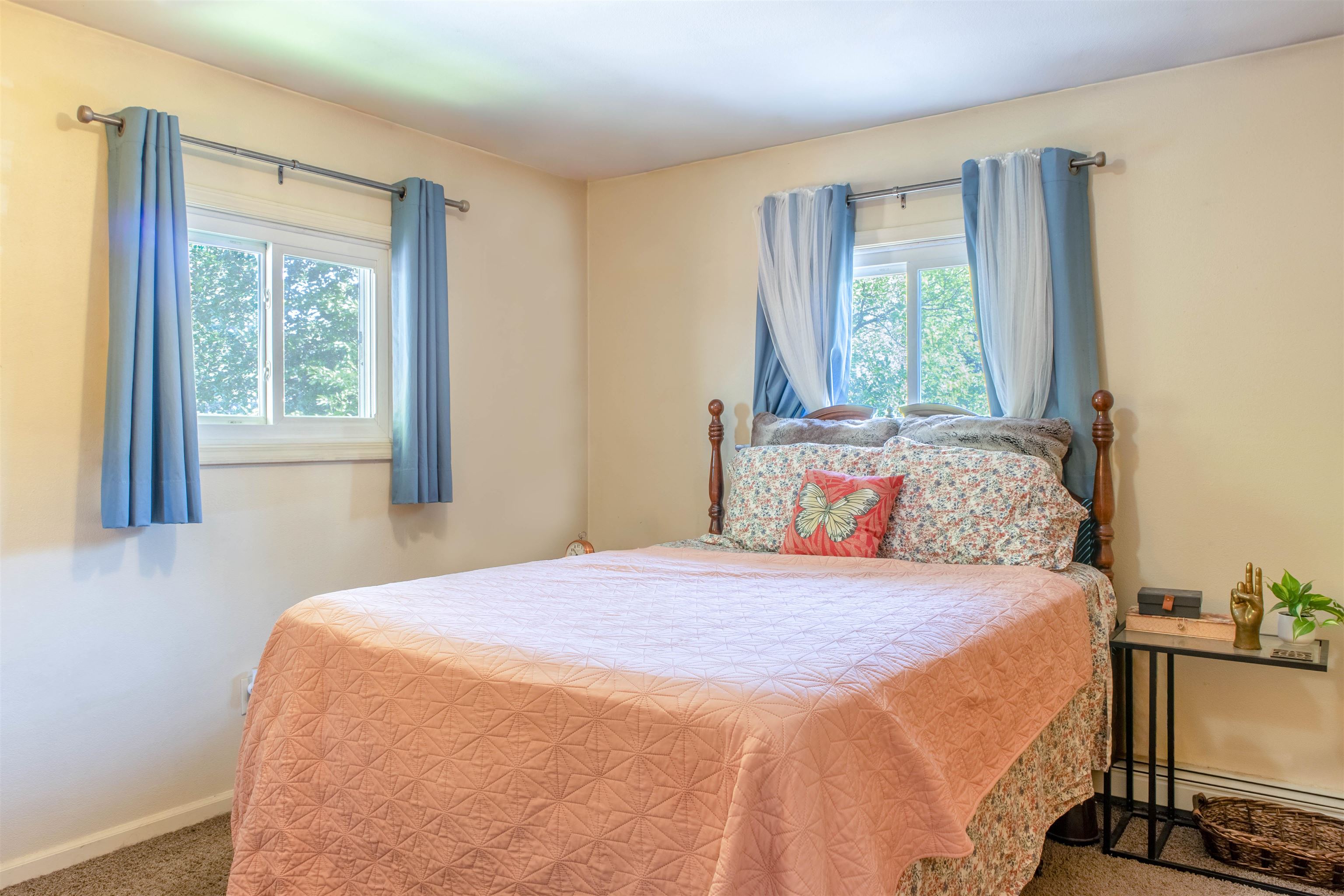 Bedroom with a peach quilted bed, floral pillows, and two windows framed by blue curtains.