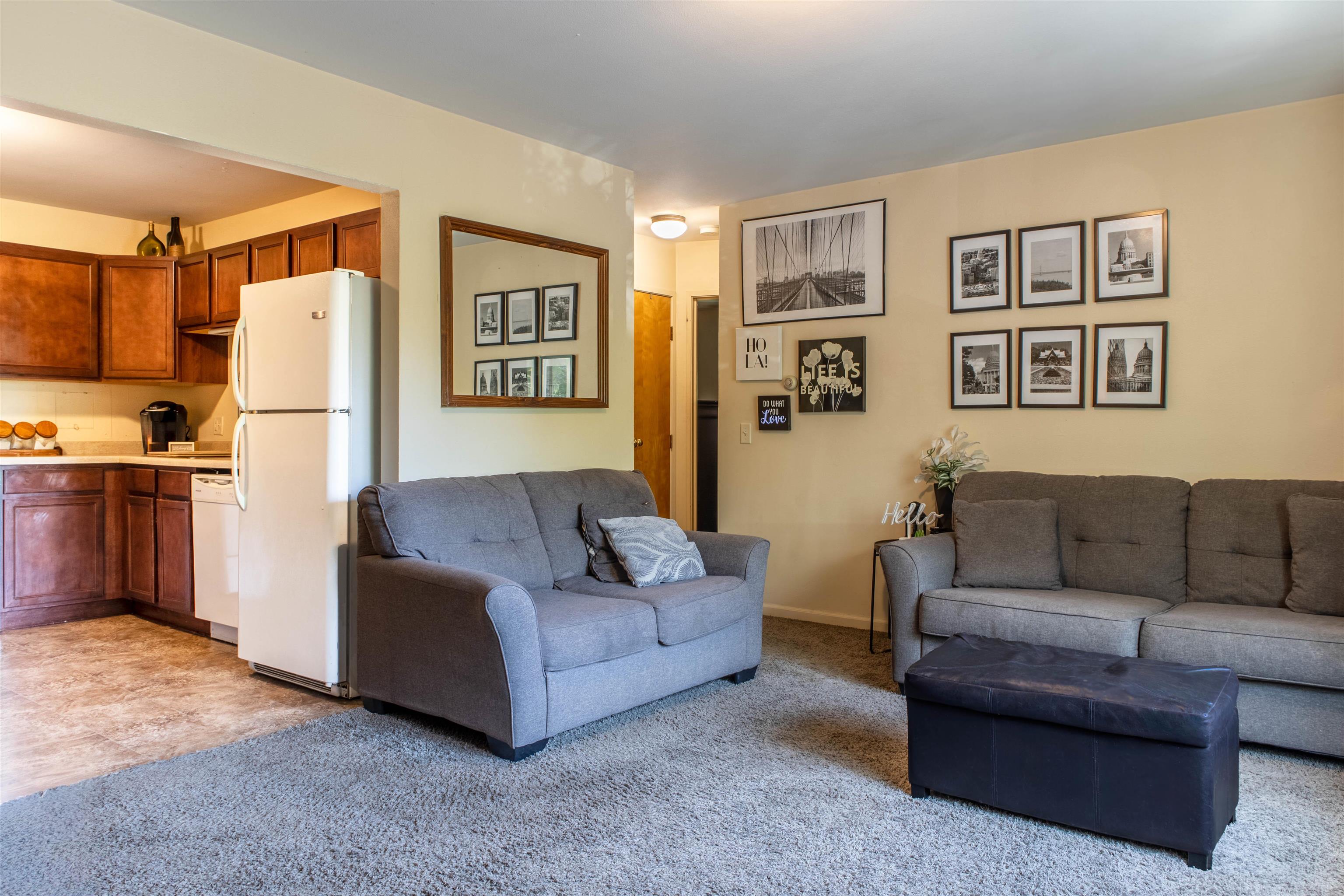Open-plan living room and kitchen with gray sofas, dark wood cabinets, and a white refrigerator.