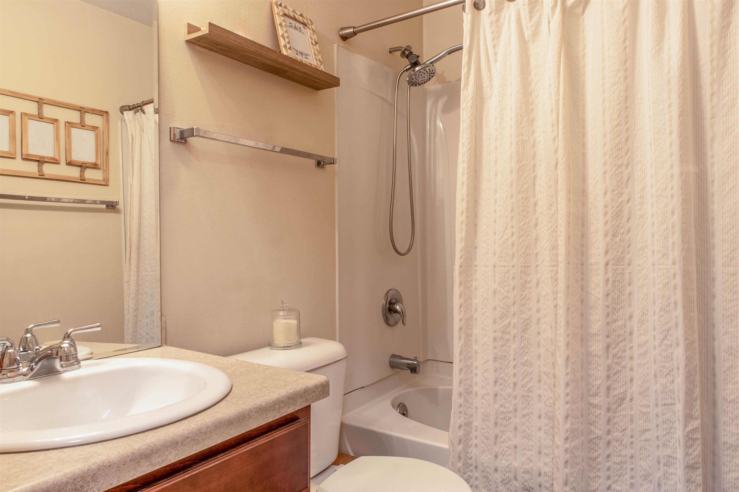 Bathroom with a wood vanity, white sink, and tub with handheld showerhead and curtain.