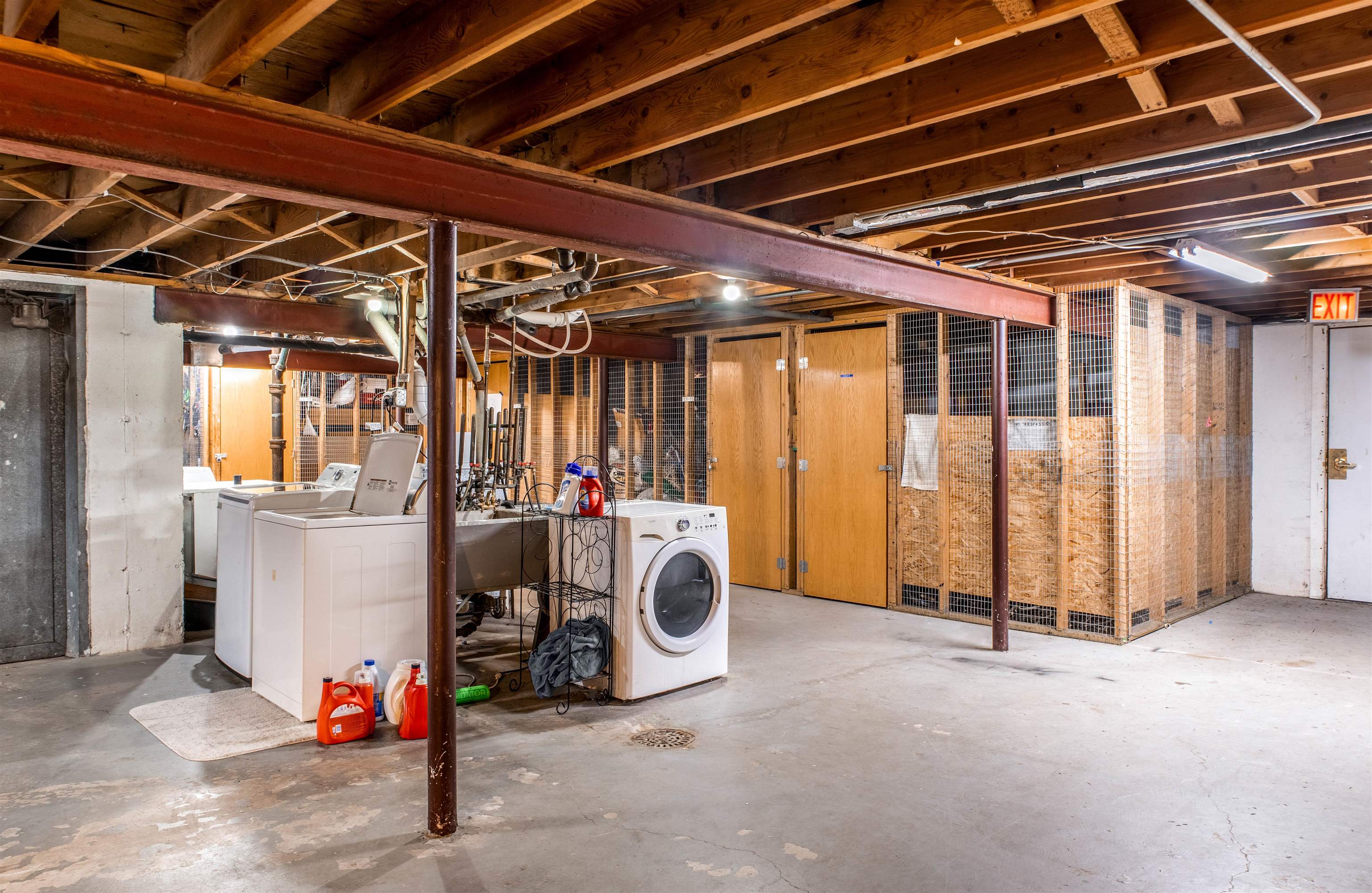 Basement laundry area with washer, dryer, utility sink, and wire storage cages.