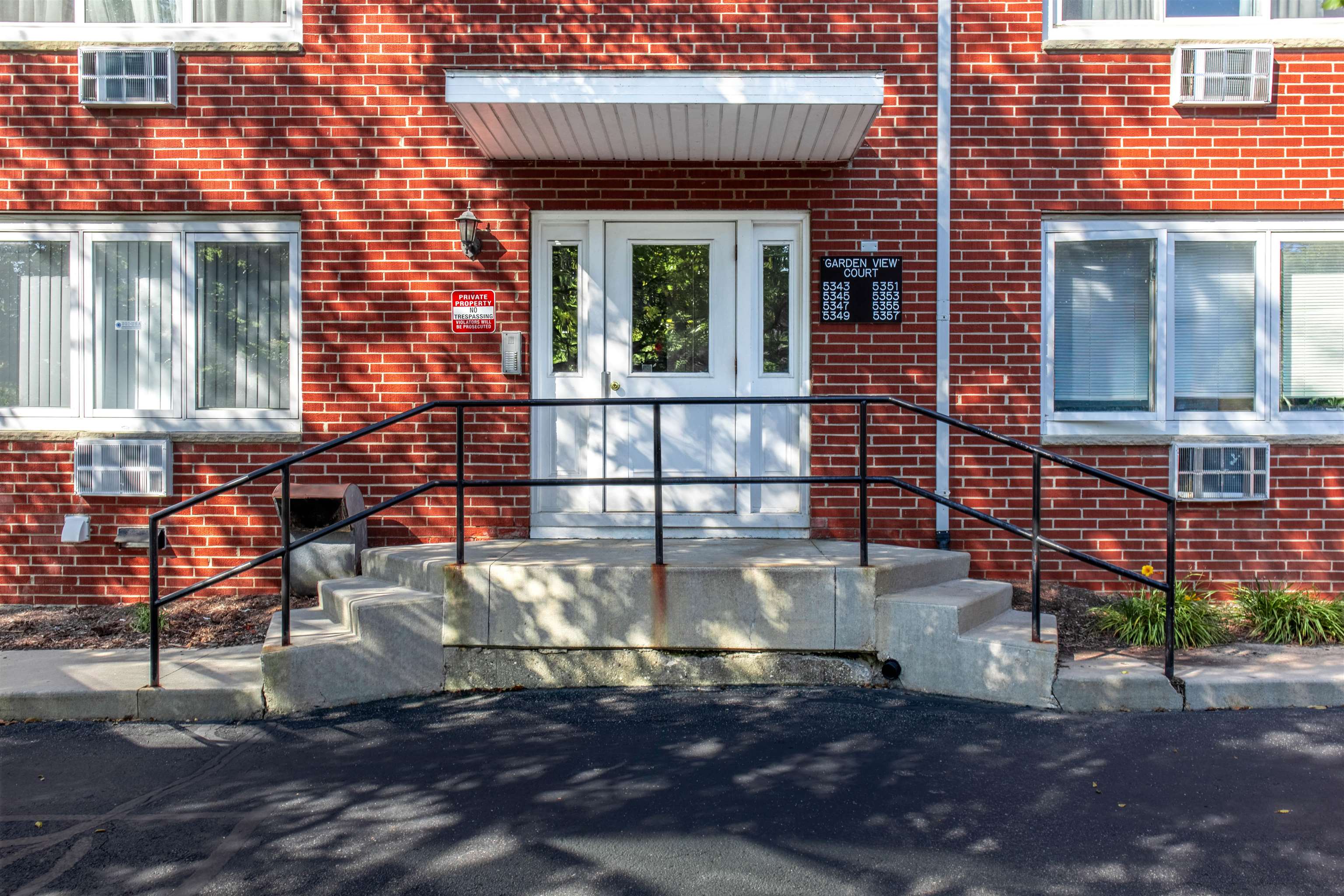 Red-brick apartment entrance with white double doors, concrete steps, and black railings.
