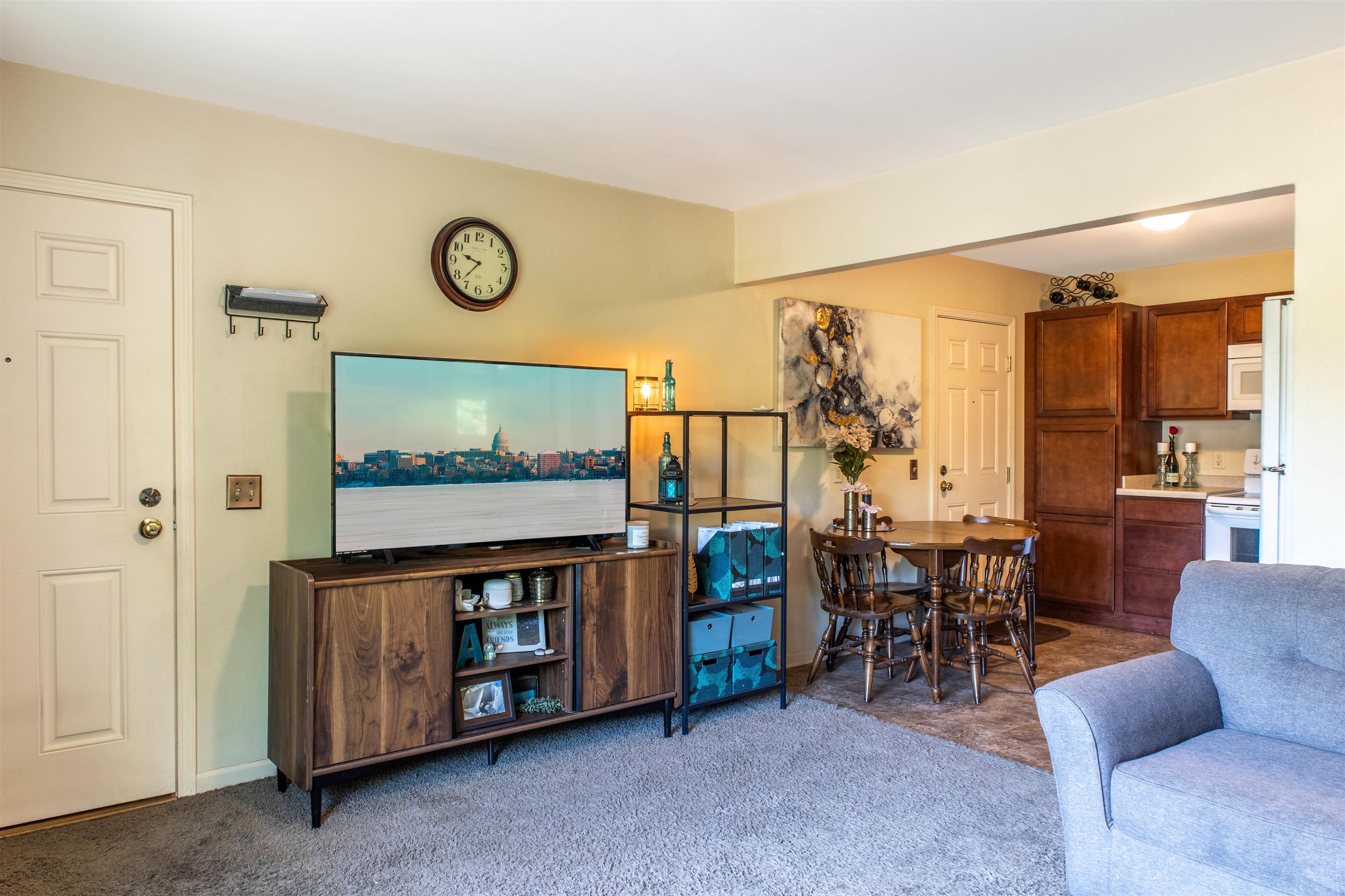 Furnished living room with a gray sofa, wooden media cabinet, and adjoining dining area and kitchen.