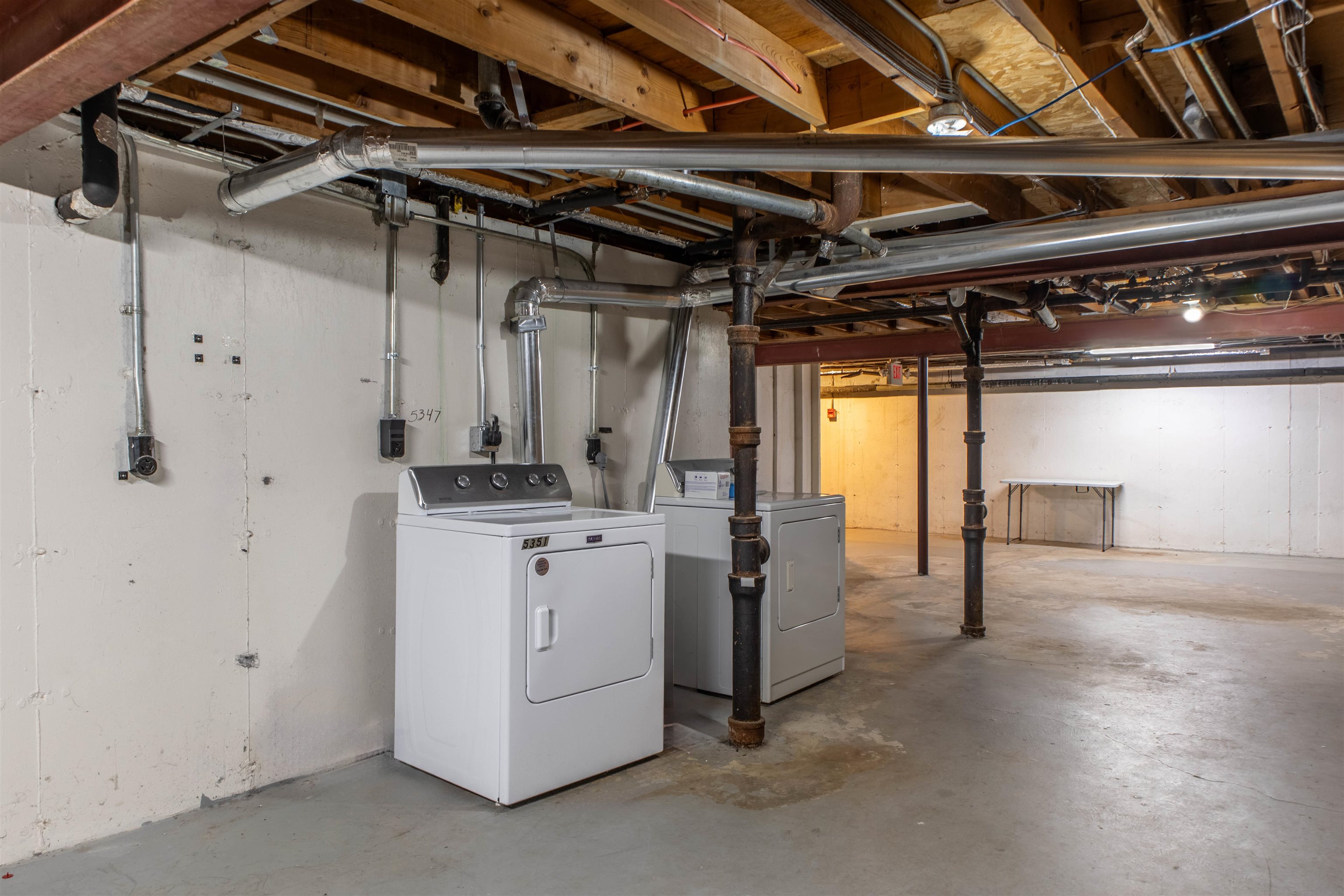 Basement laundry area with a white washer and dryer beneath exposed joists and pipes.