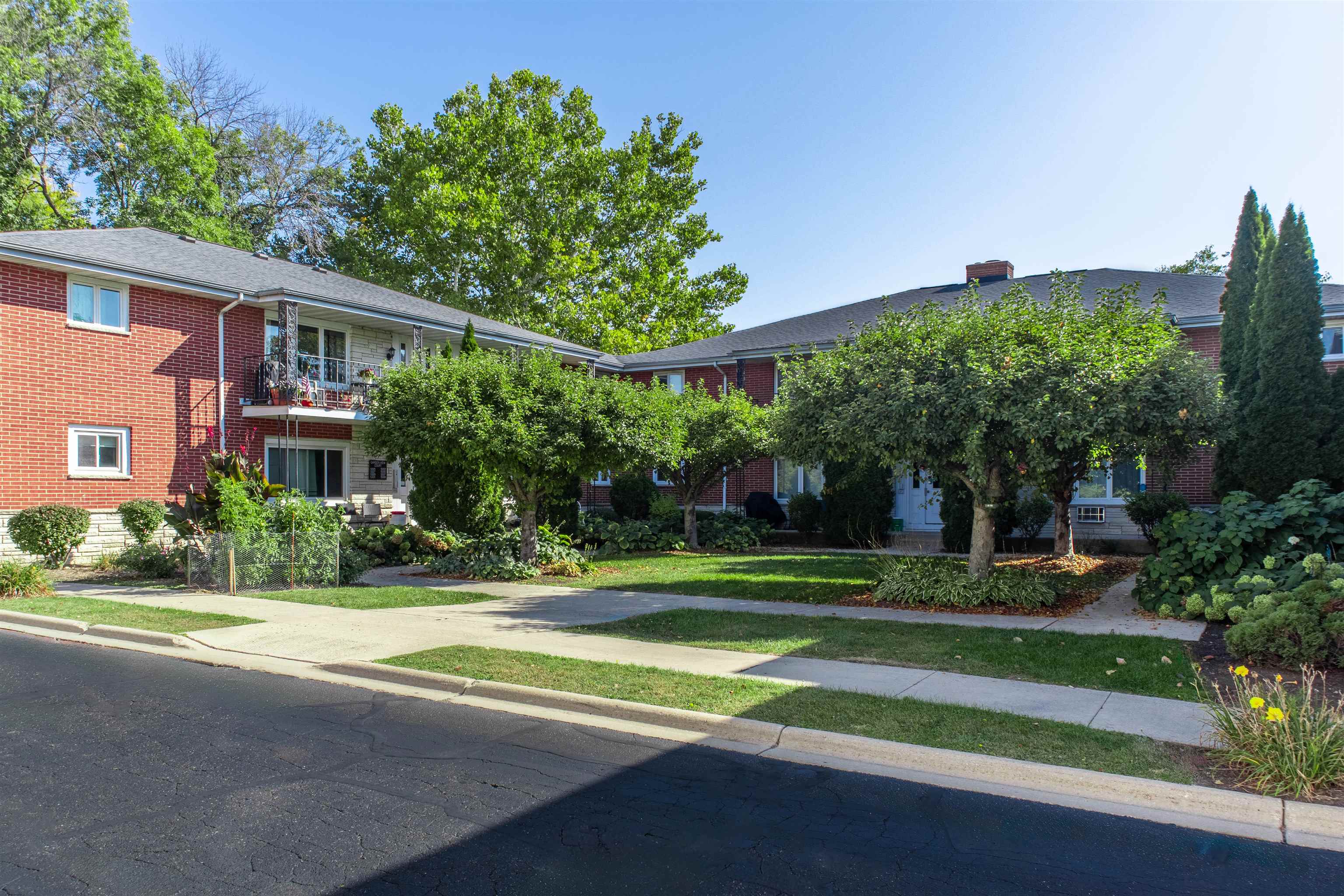 Red-brick residential building with a landscaped courtyard, mature trees, and a small balcony.