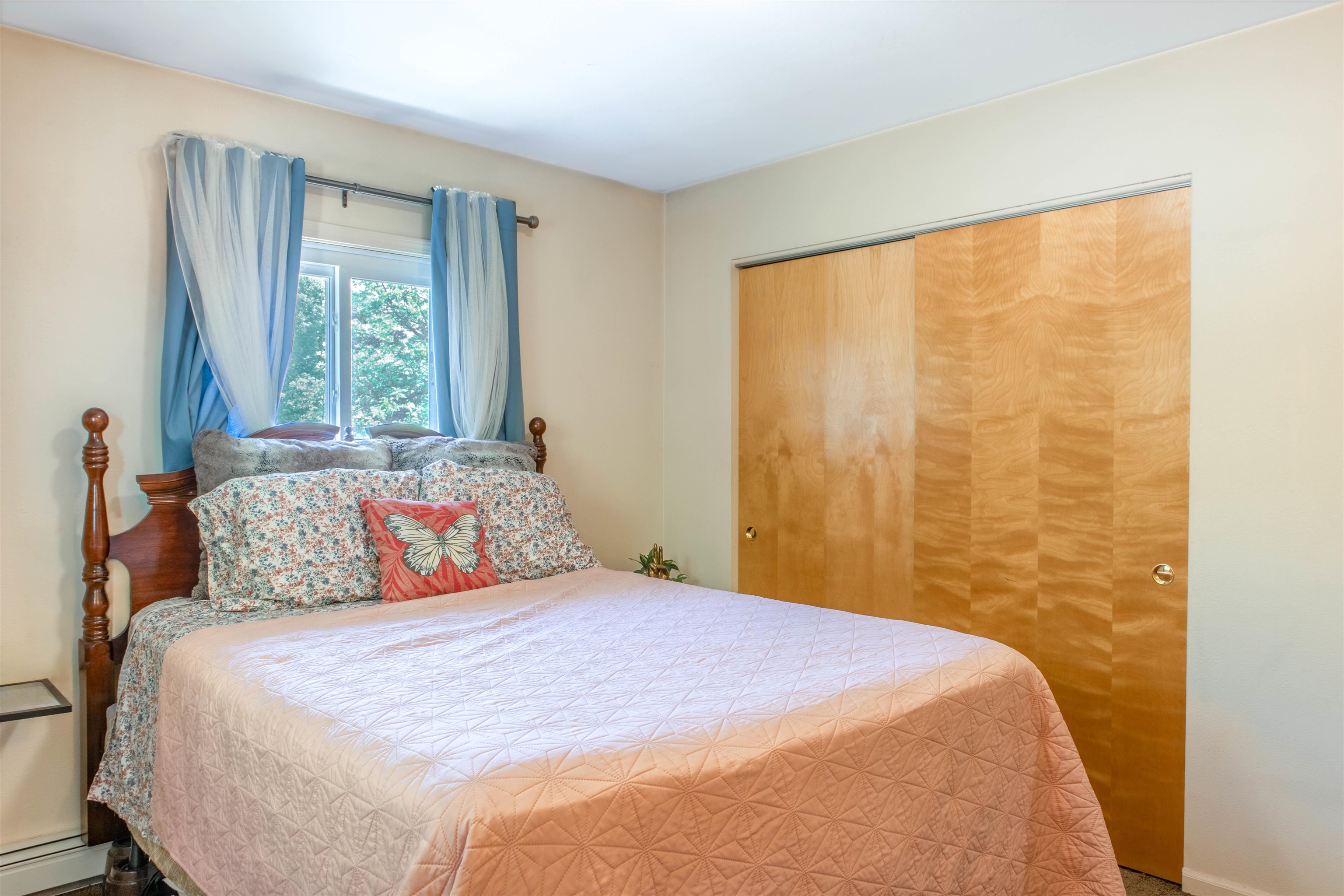 Bedroom with a quilt-covered bed, blue curtains, and wooden sliding closet doors.