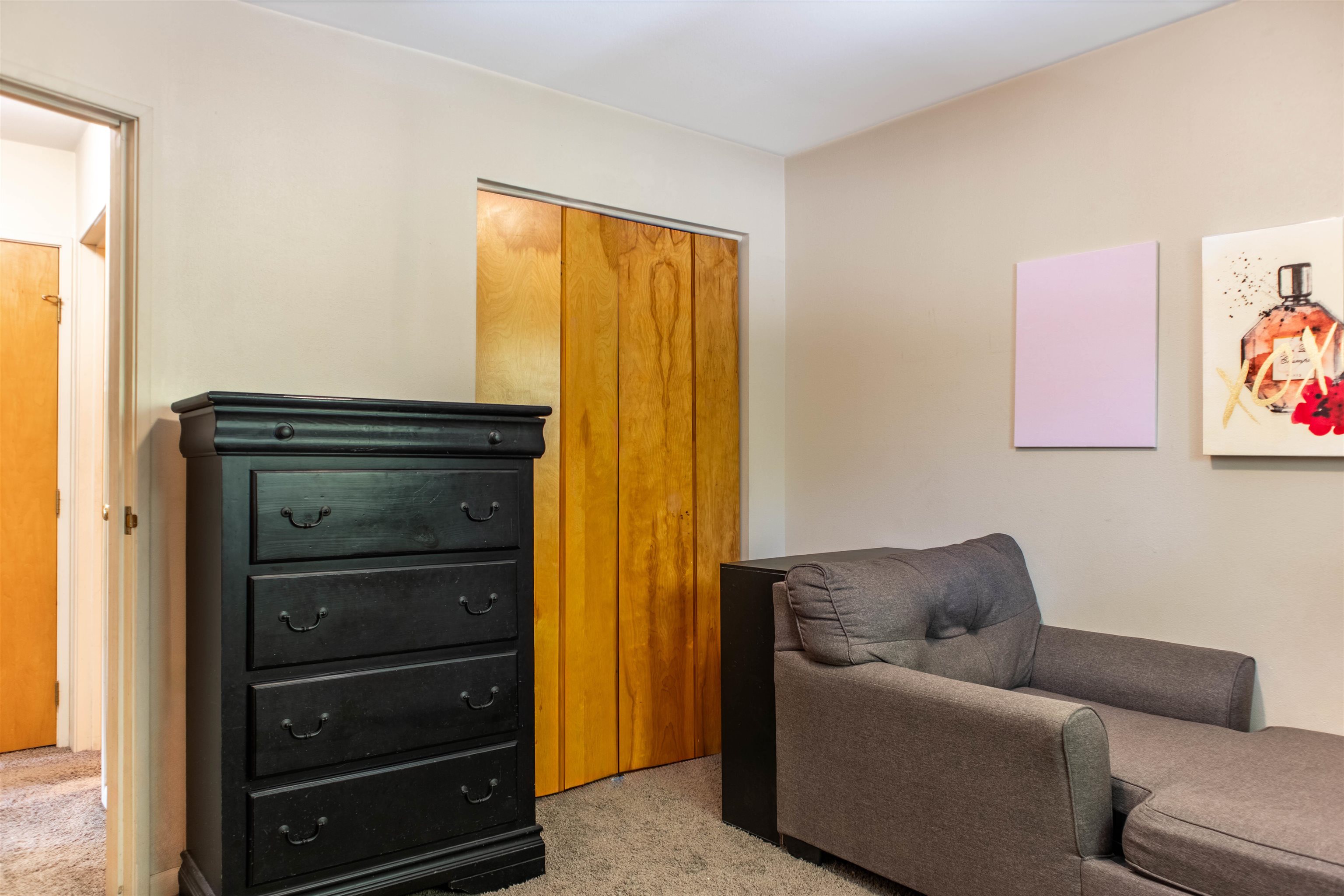 Furnished bedroom with a gray sofa, black dresser, and wooden closet doors.