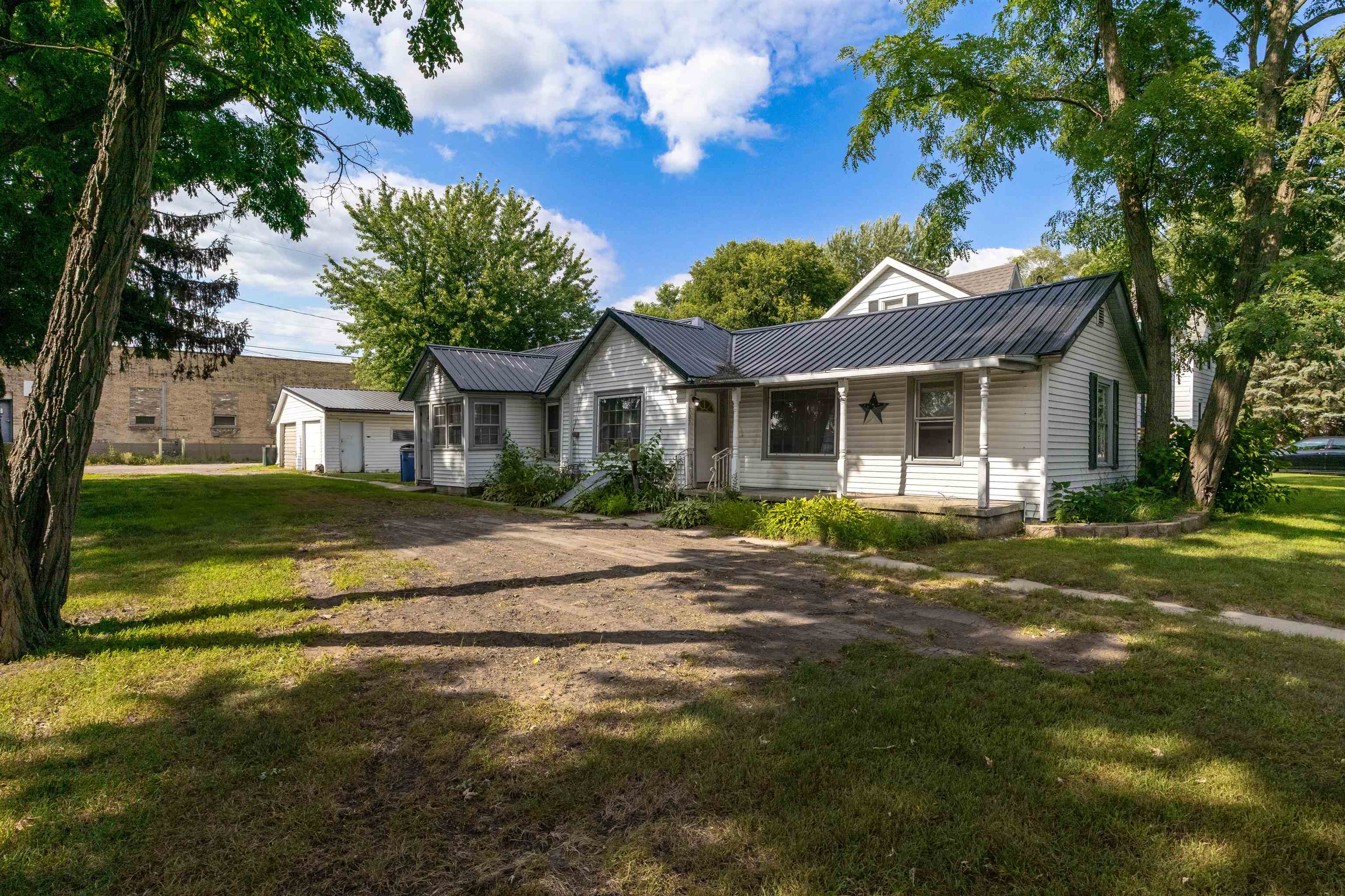 White single-story house with a dark metal roof, detached garage, and shaded yard.