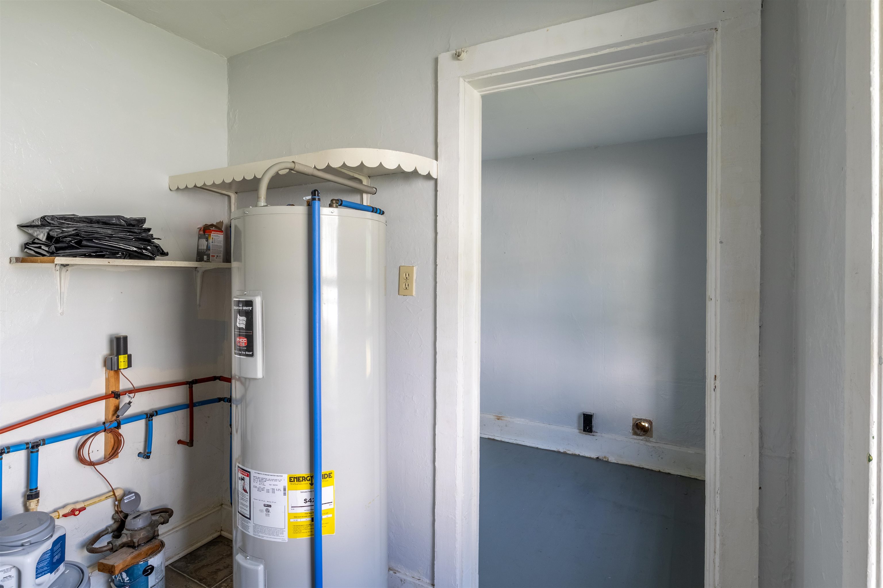 Utility room with a large water heater and exposed plumbing beside an open doorway.
