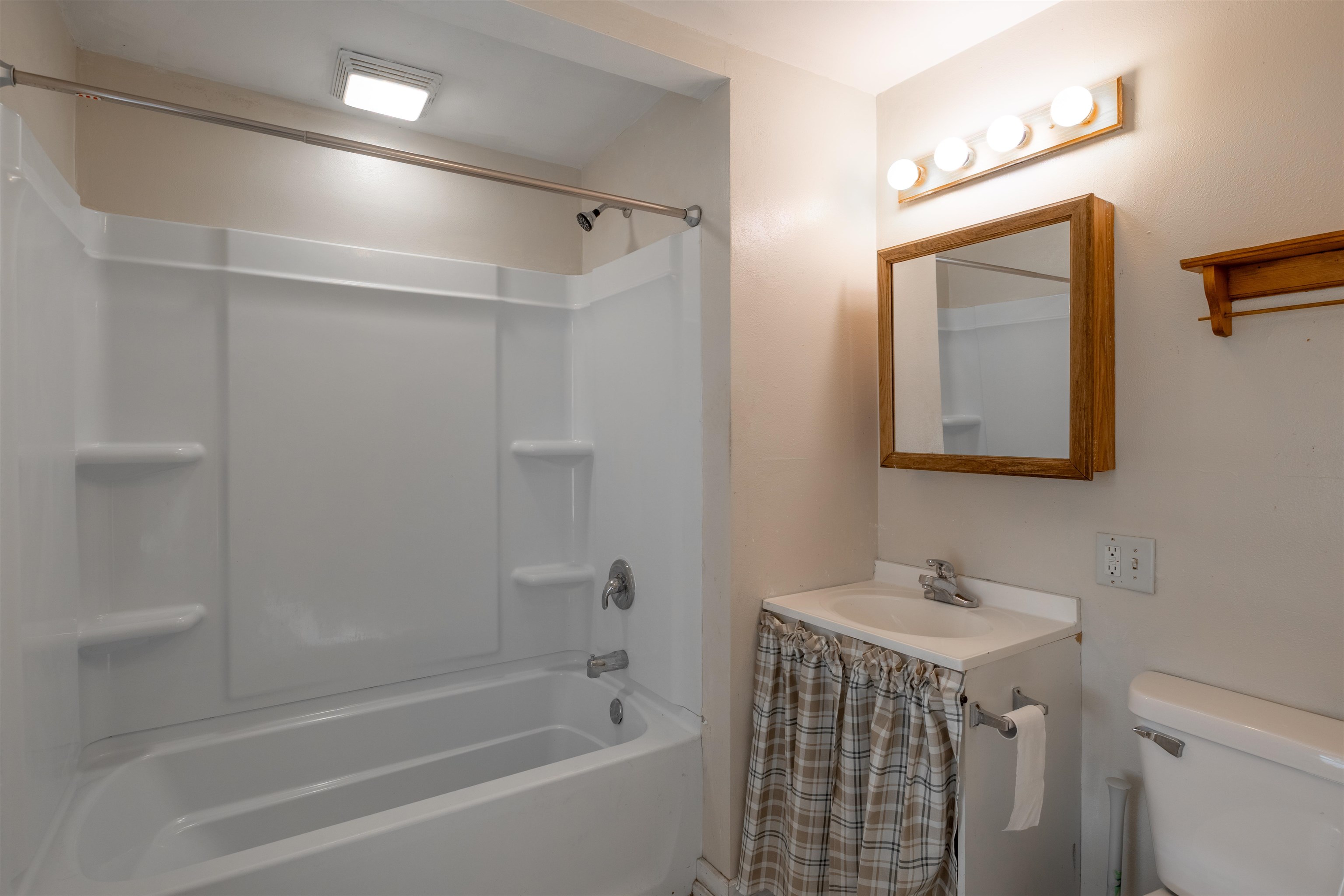 Bathroom with a white tub and shower, wood-framed mirror, and plaid vanity curtain.