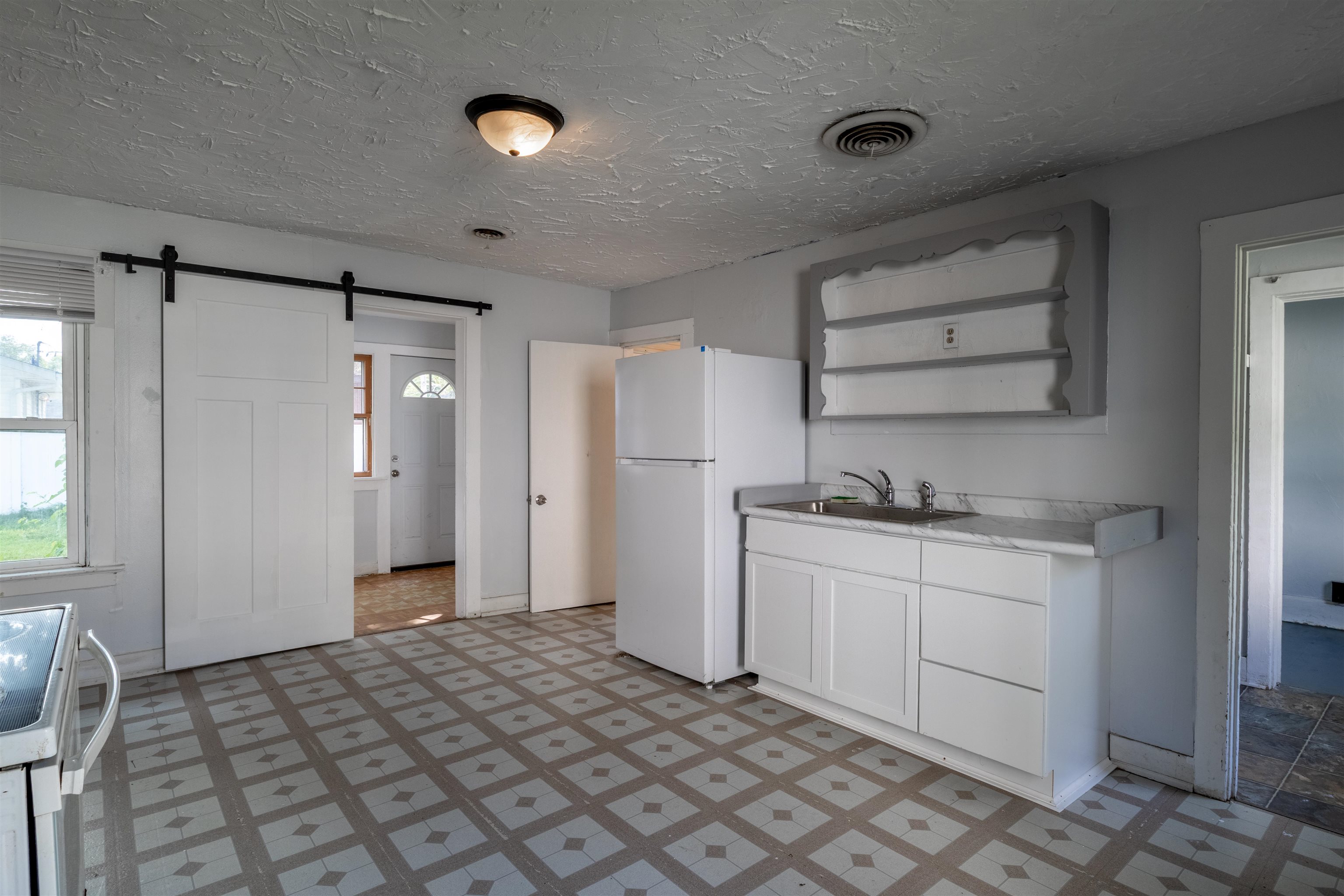 Vacant kitchen with a white refrigerator, sink, and patterned tile floor.