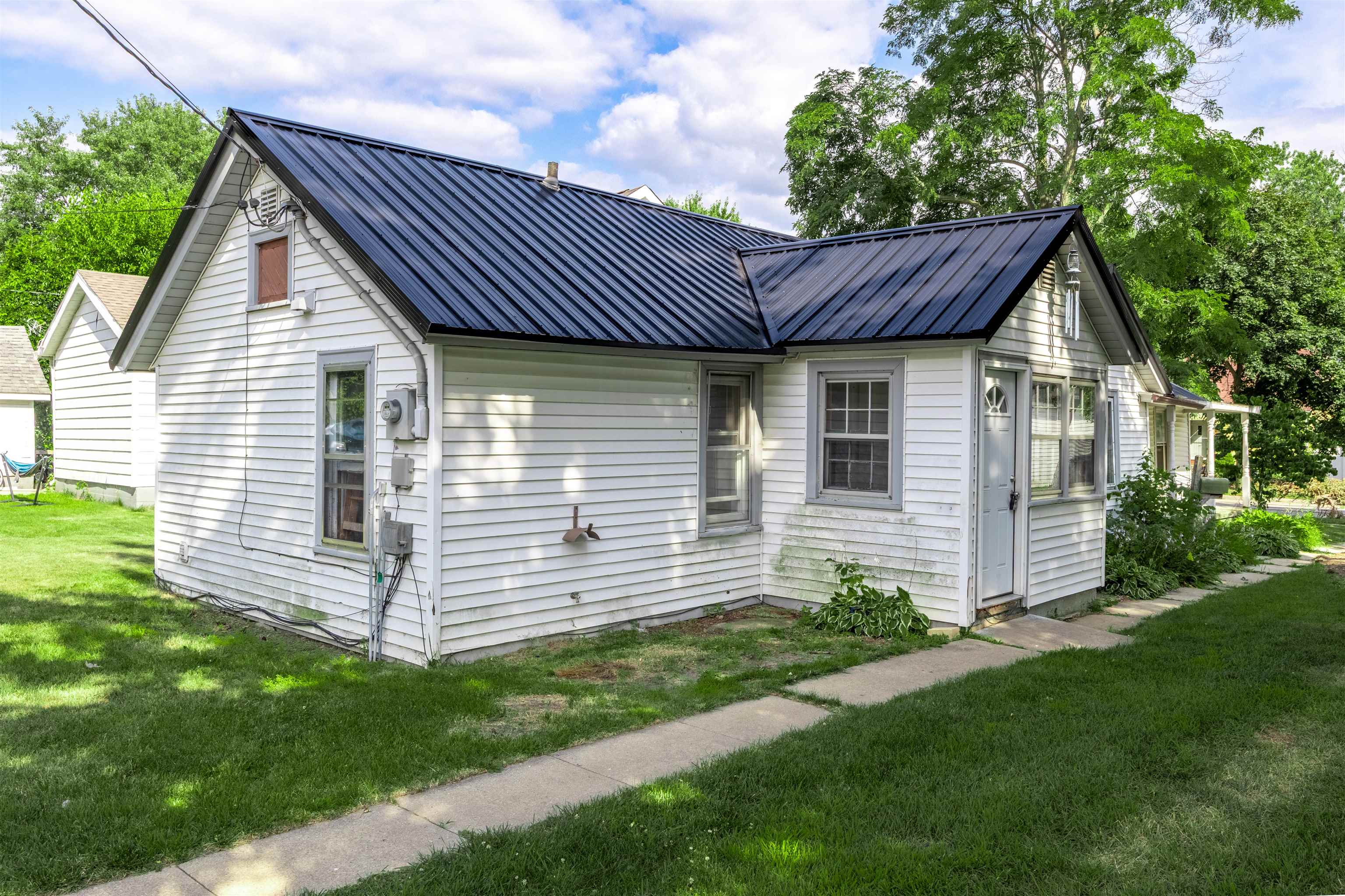 White-sided house with a dark metal roof beside a lawn and concrete walkway.