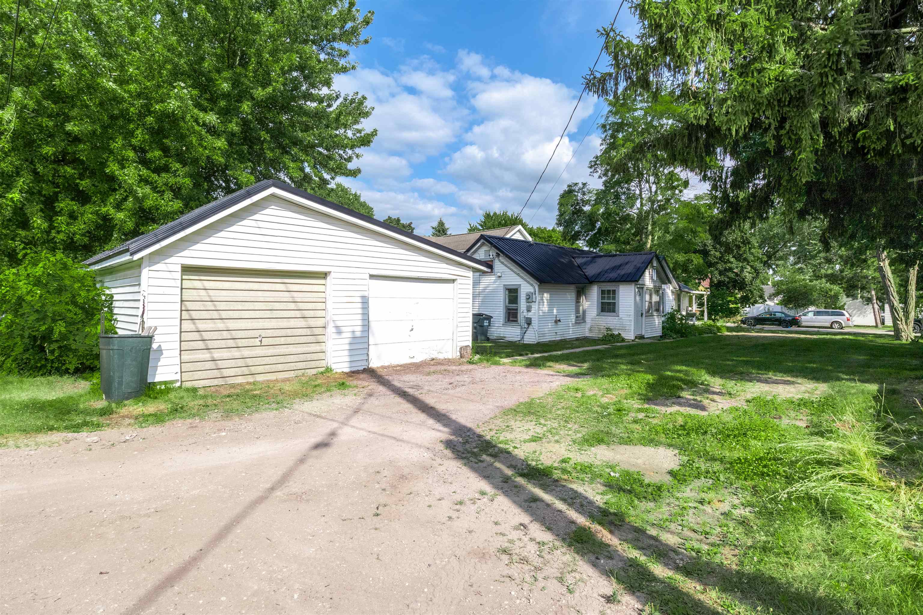 White house with a dark metal roof beside a detached garage and gravel driveway.