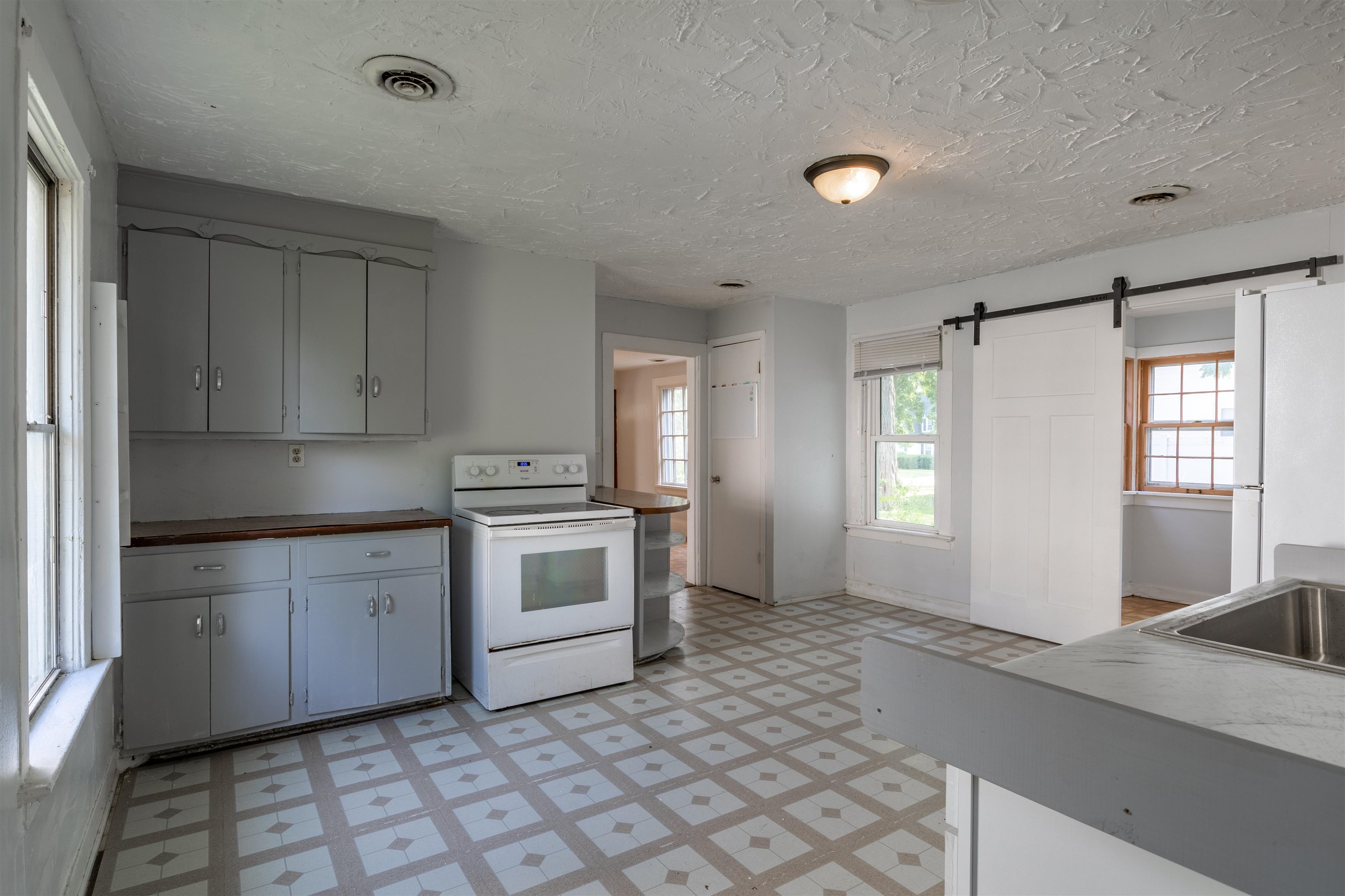 Kitchen with gray cabinets, a white electric range, patterned tile floor, and a sliding barn door.