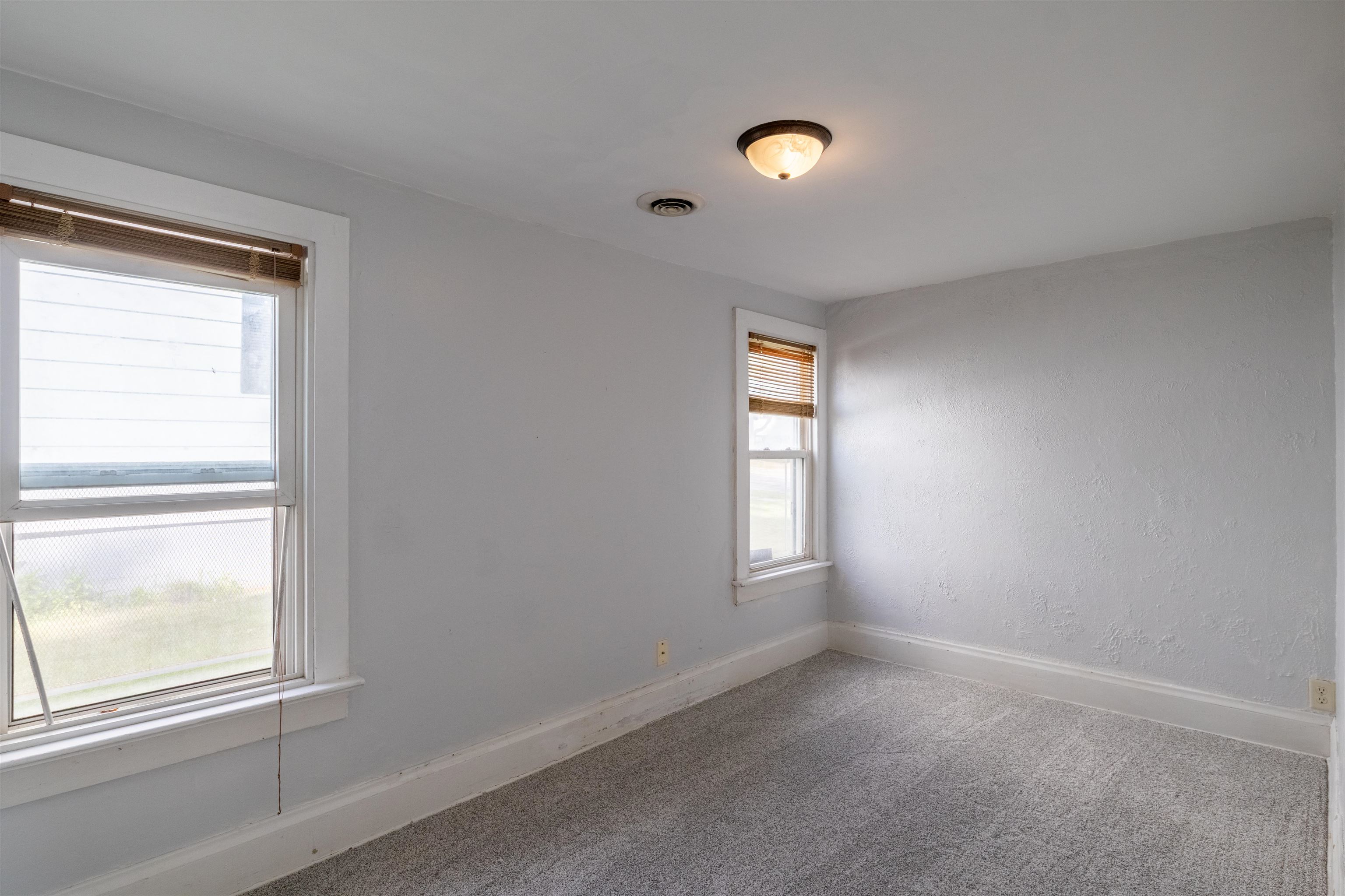 Empty carpeted room with gray walls and two windows with wooden blinds.