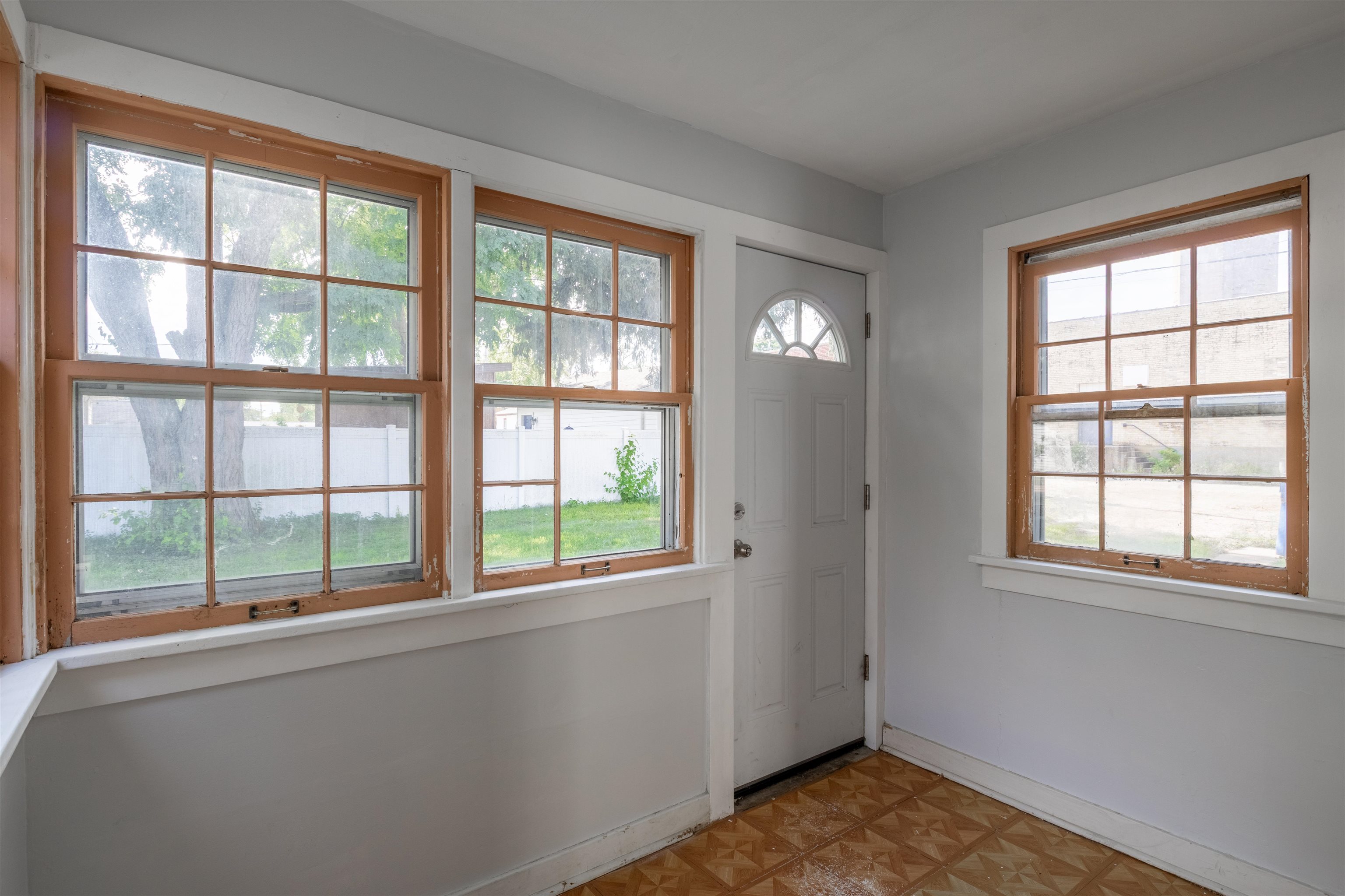 Empty entry room with large wood-trimmed windows, a white exterior door, and patterned wood flooring.