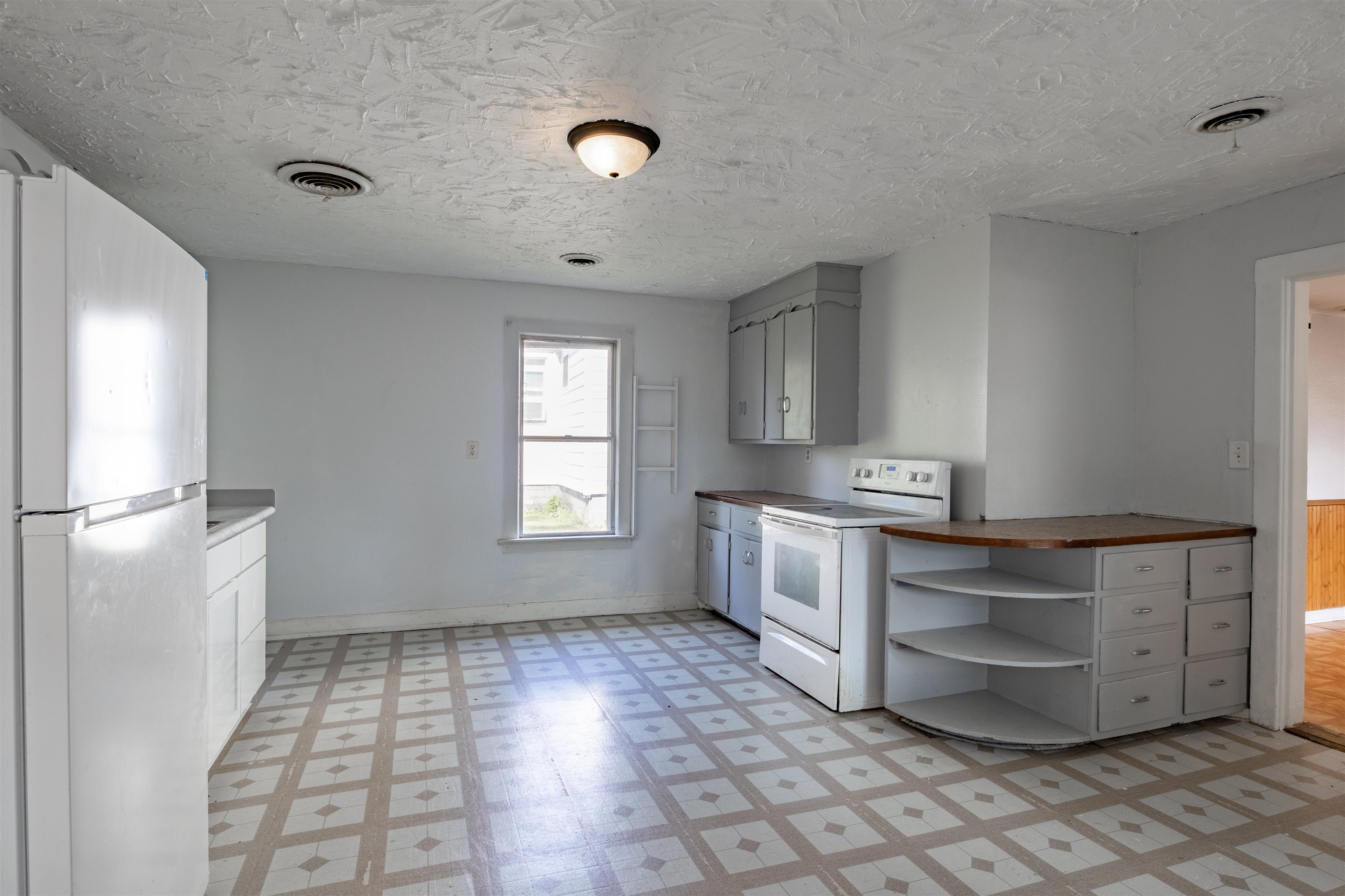Vacant kitchen with gray cabinets, white appliances, a curved peninsula, and geometric patterned flooring.