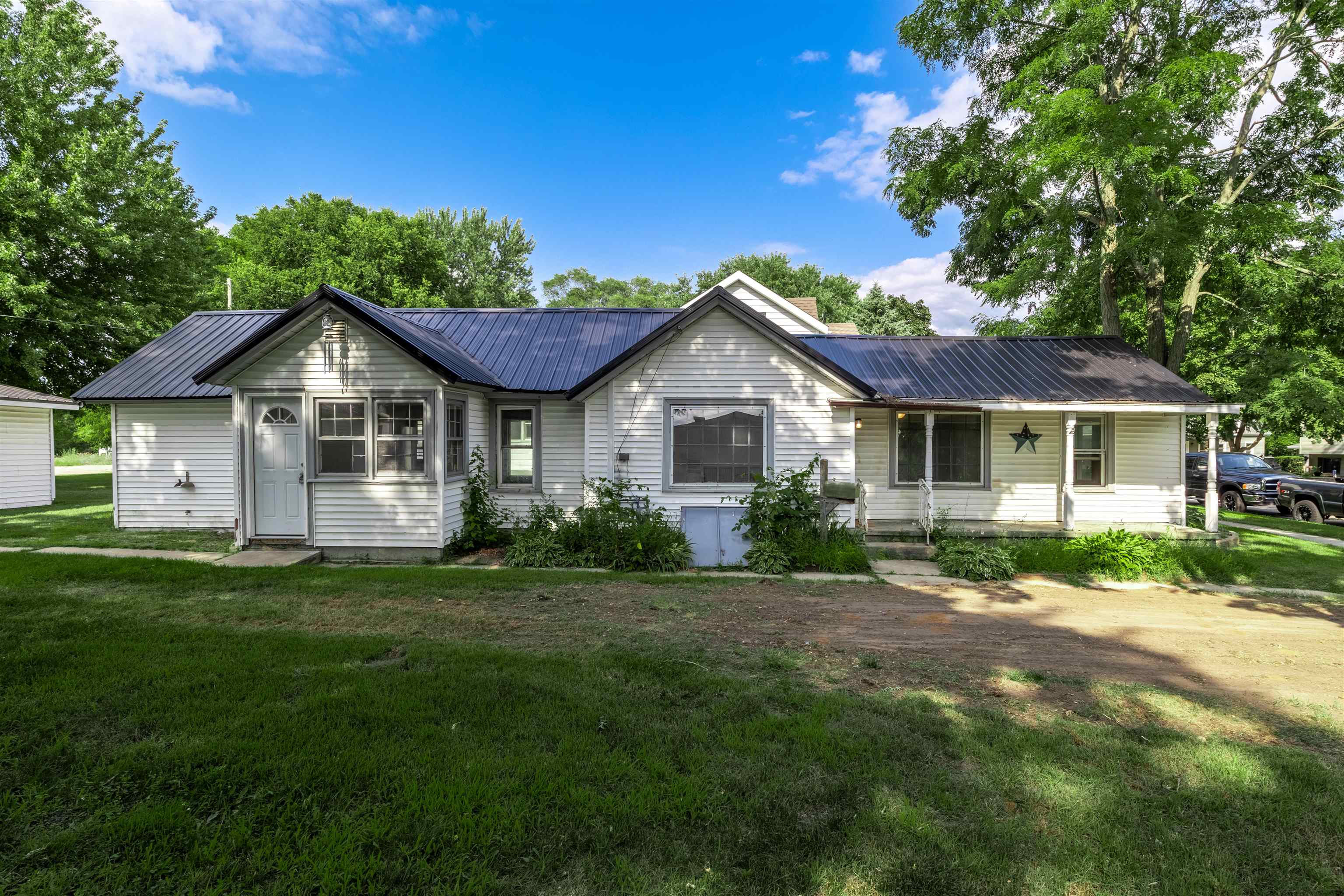 Single-story white house with a dark metal roof, covered entry, and grassy front yard.