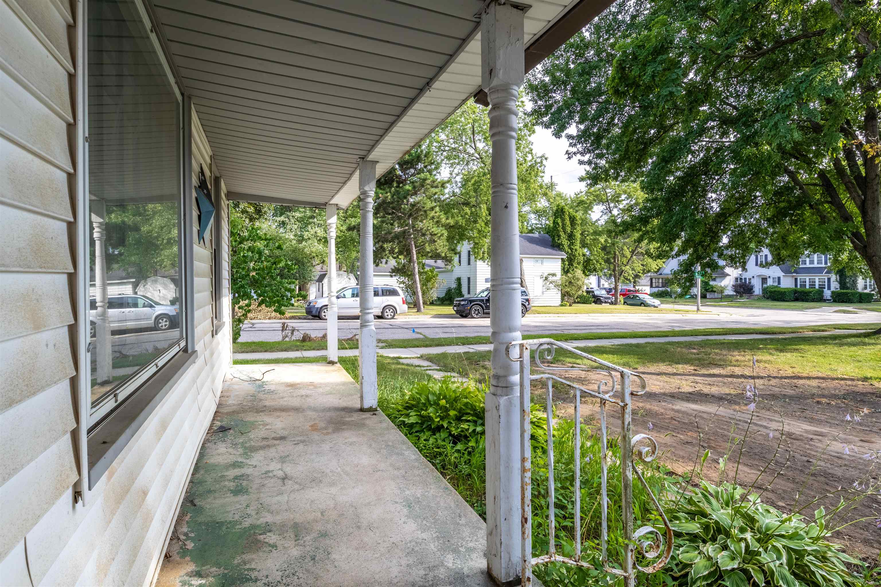 Covered front porch with white turned columns, decorative metal railing, and a leafy yard.