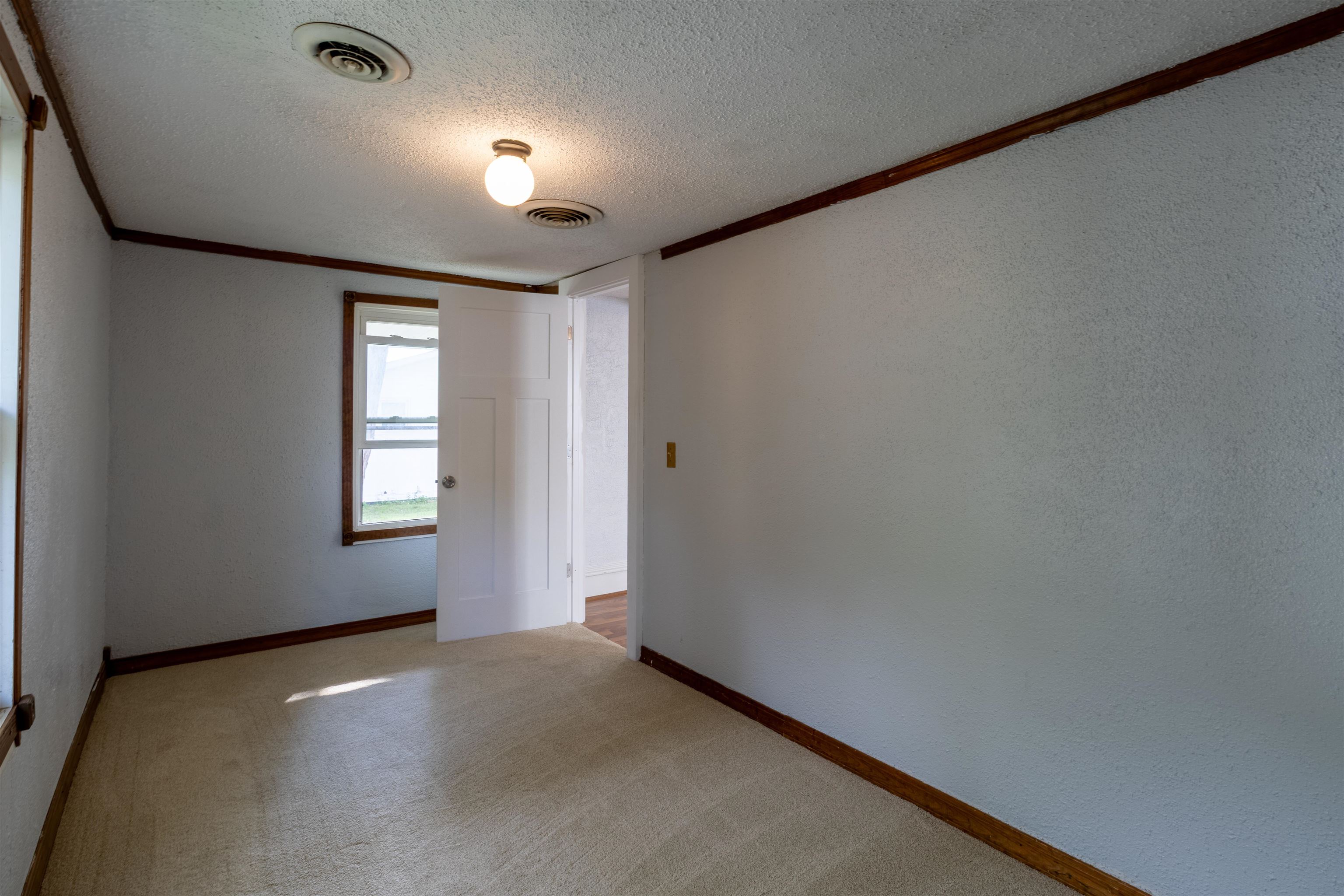Empty carpeted room with dark wood trim, a window, and an open door.