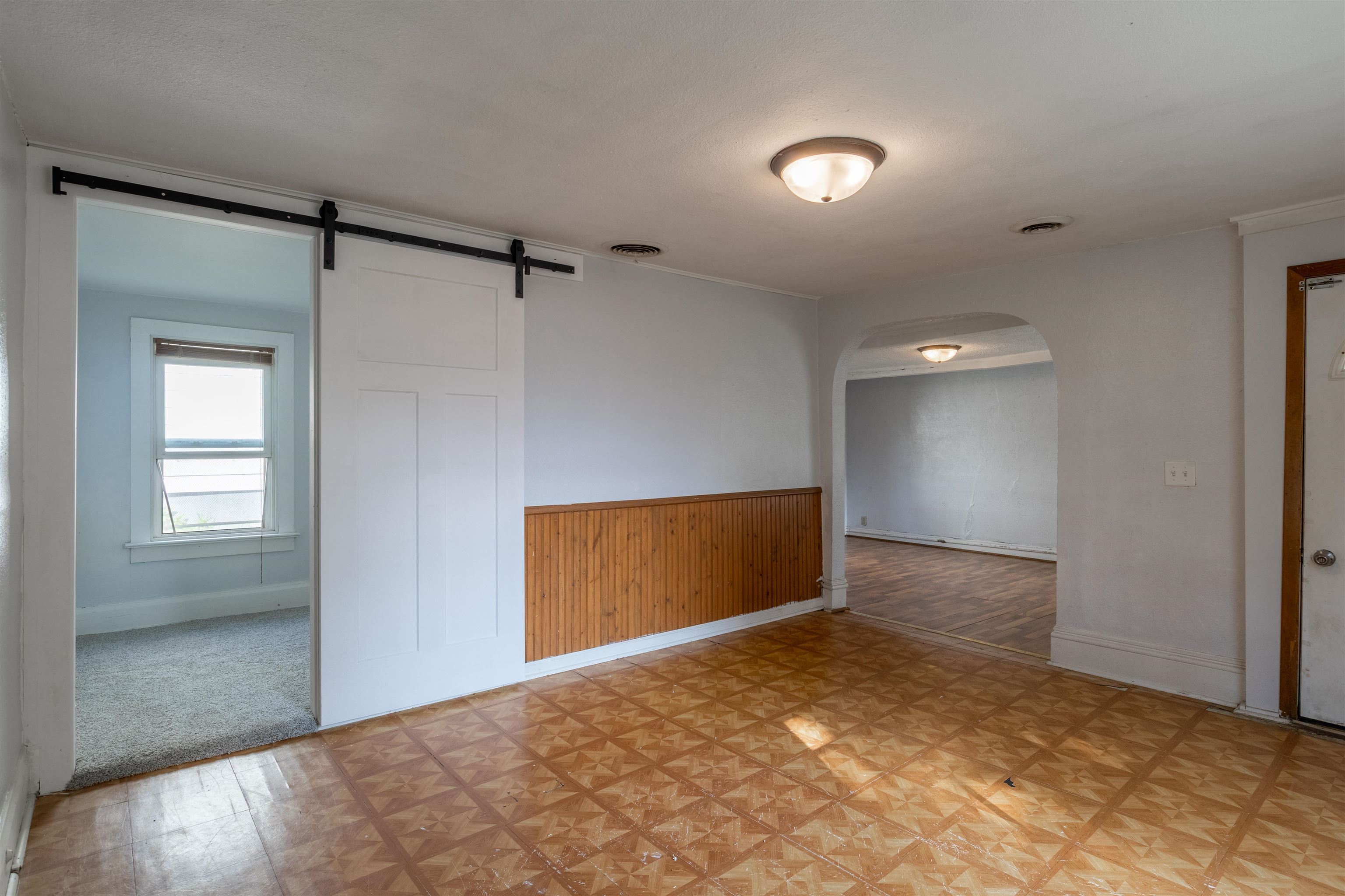 Vacant room with patterned flooring, wood wainscoting, a sliding barn door, and an arched opening.