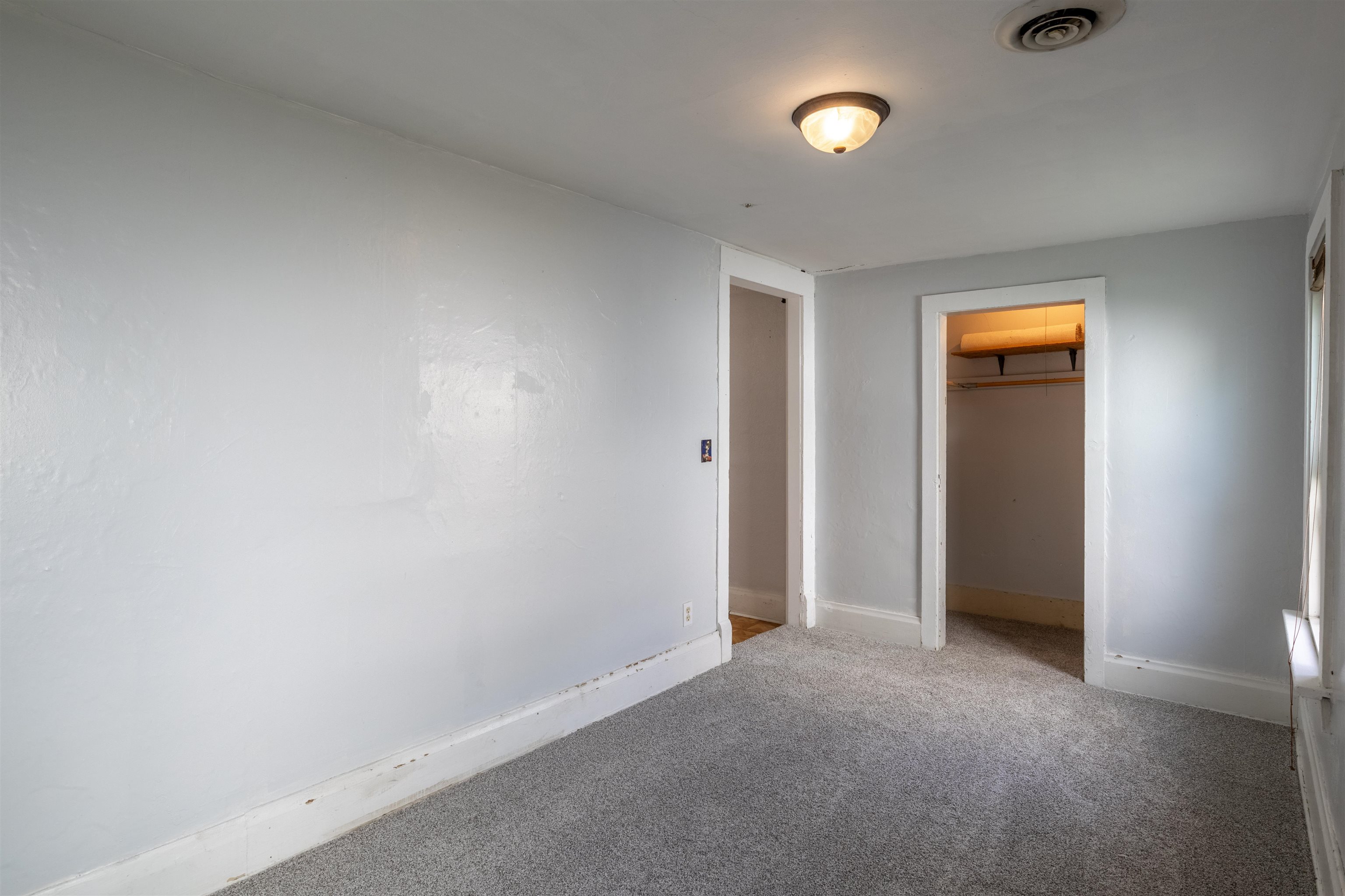 Empty bedroom with gray carpet and an open closet with a shelf and hanging rod.