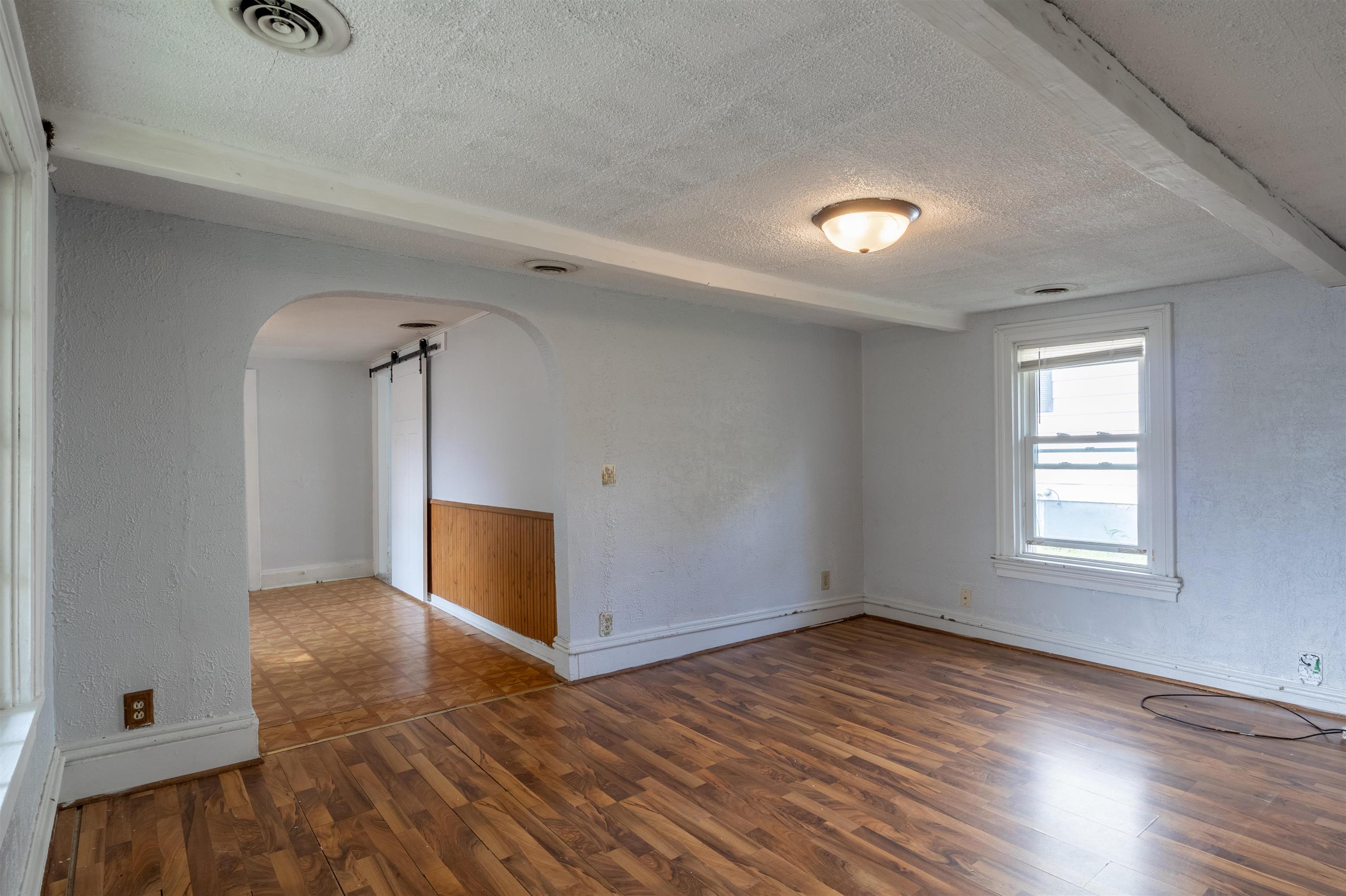 Empty living room with wood-look floors, a bright window, and an arched opening to a tiled area.