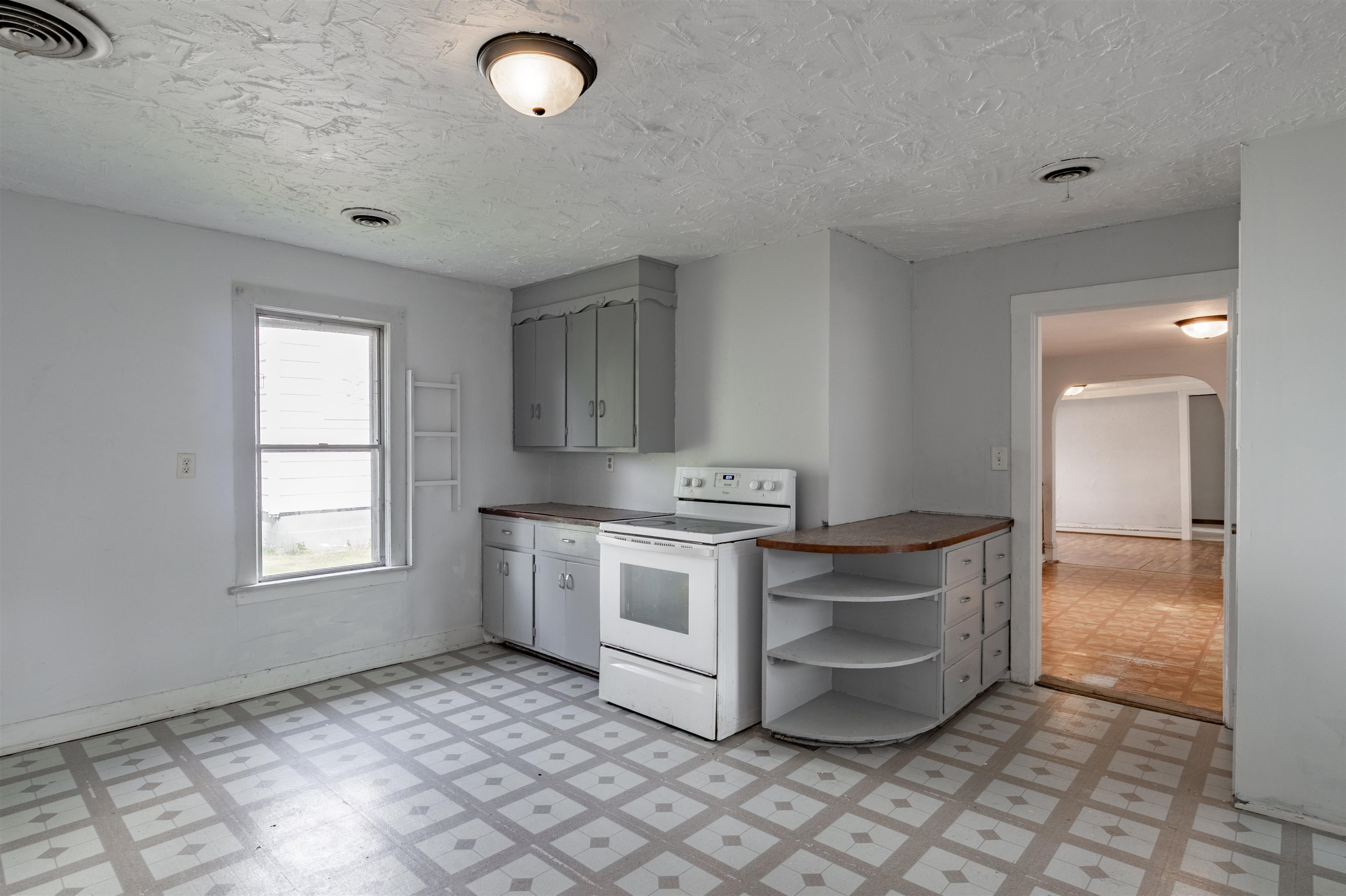 Vacant kitchen with white cabinets, a freestanding stove, curved counter, and patterned tile floor.