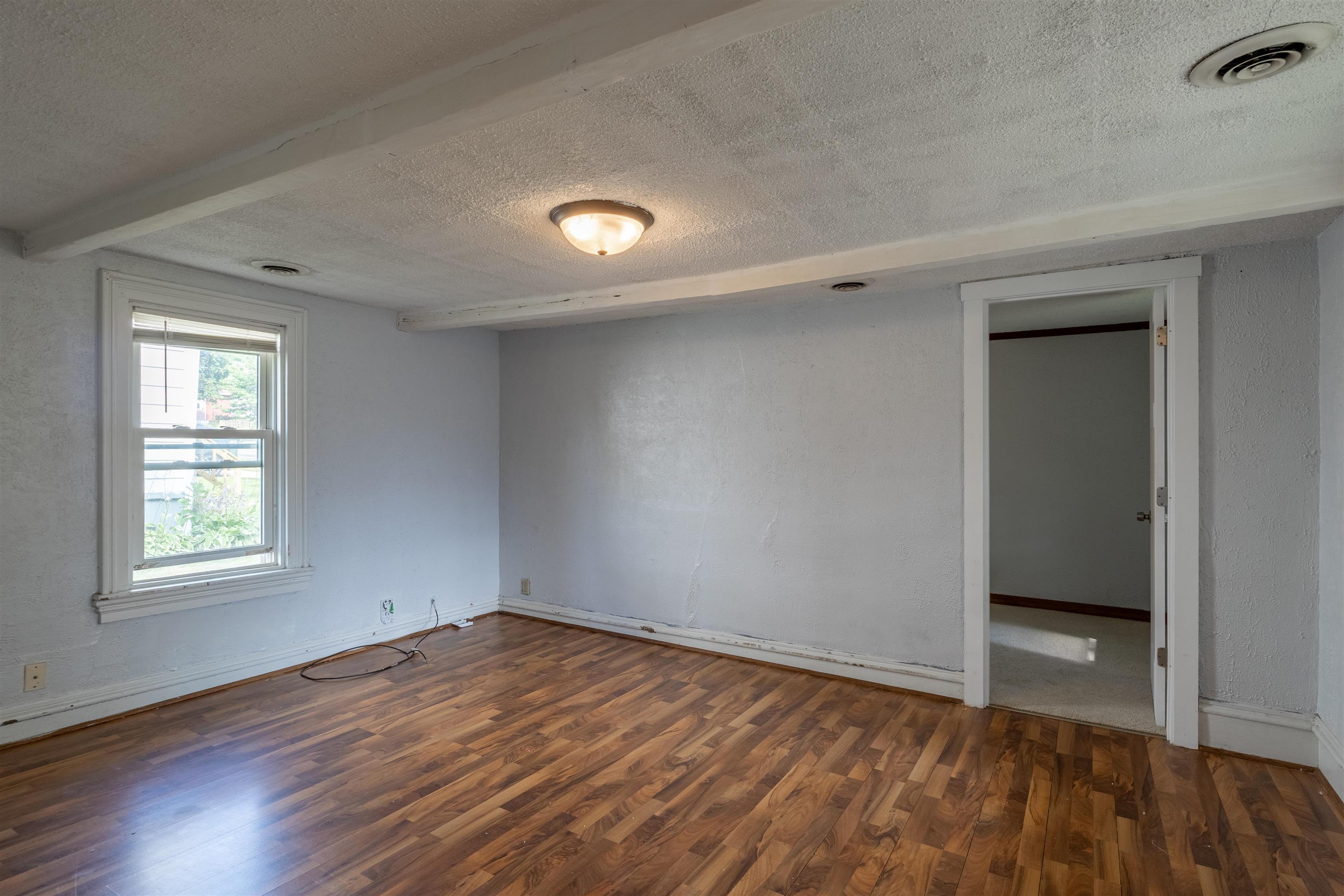 Empty room with brown plank flooring, a window with blinds, and an open doorway.