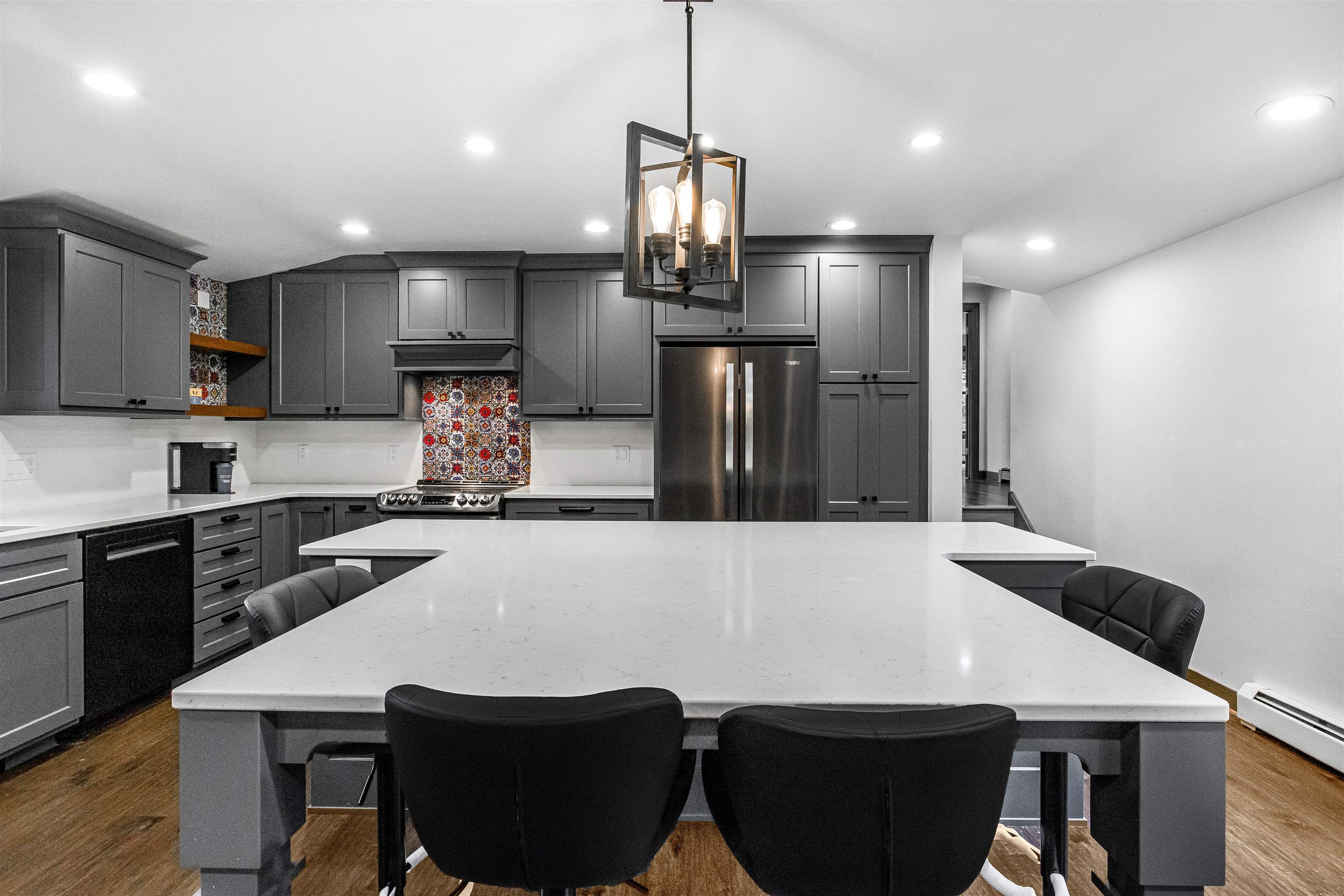 Modern kitchen with dark gray cabinets, patterned tile backsplash, and a large white island.