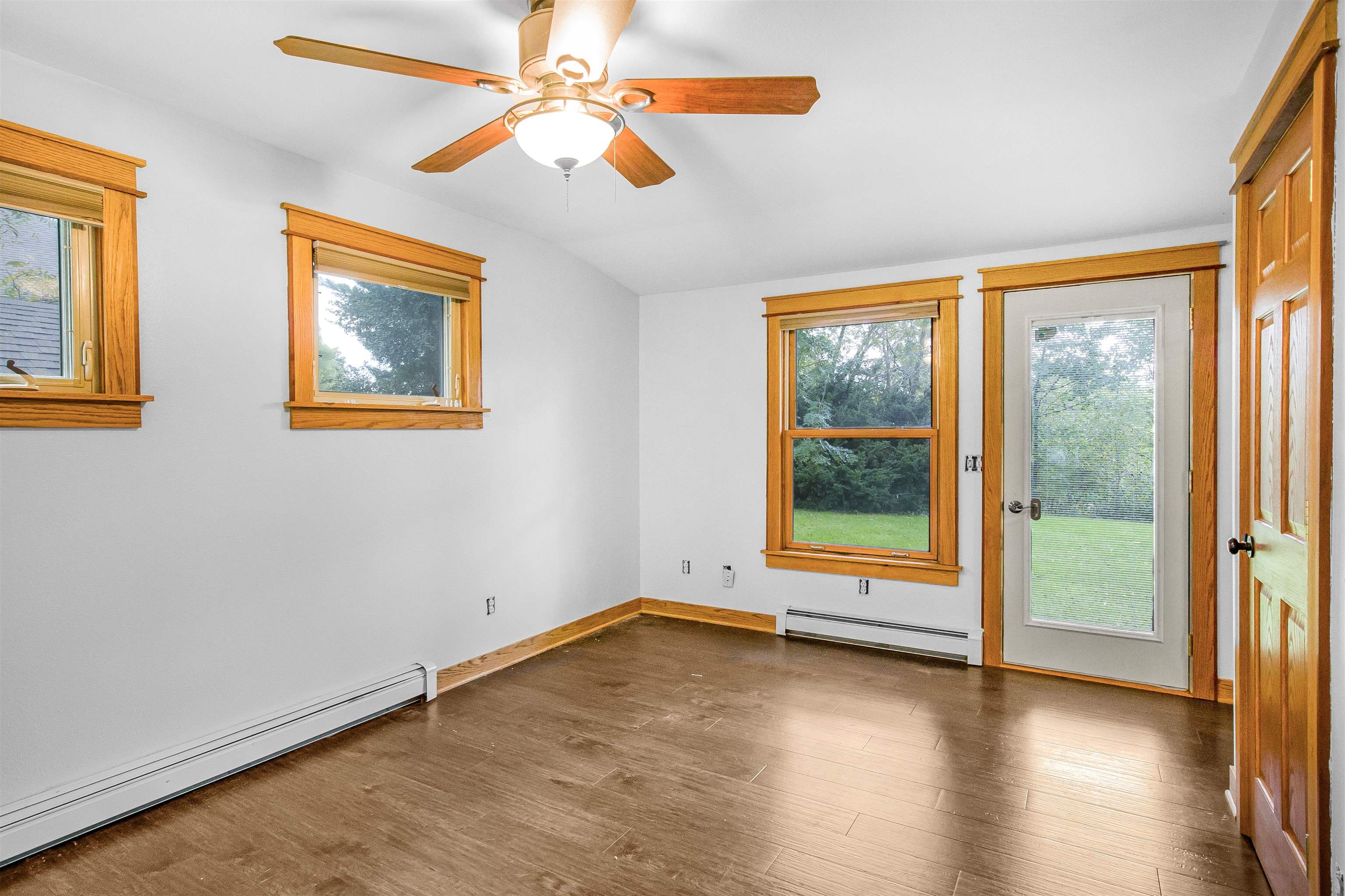 Empty room with dark flooring, wood-trimmed windows, a glass door, and a ceiling fan.
