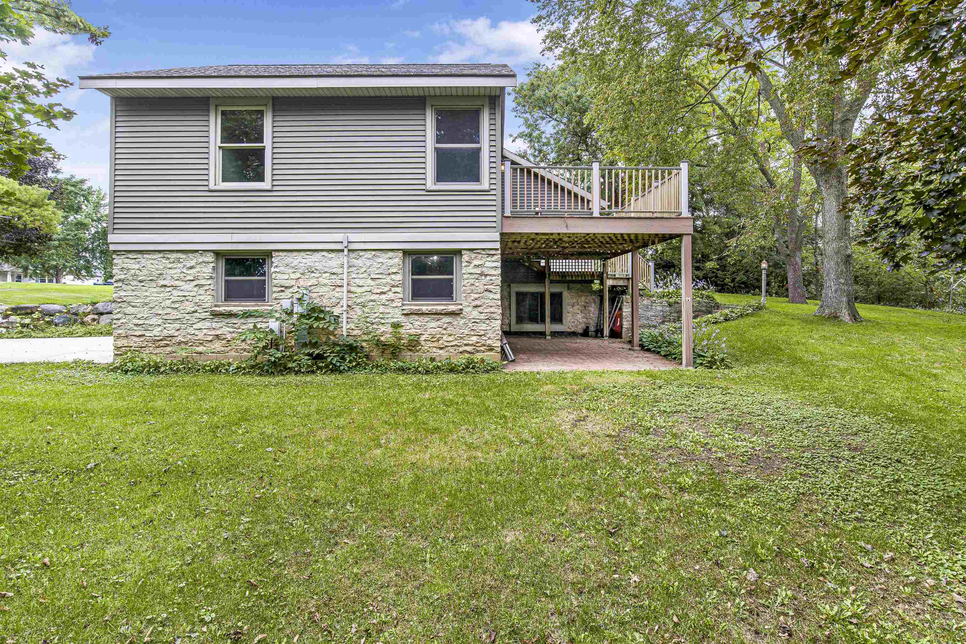 Rear of a gray-sided house with a raised deck, stone lower level, and grassy yard.