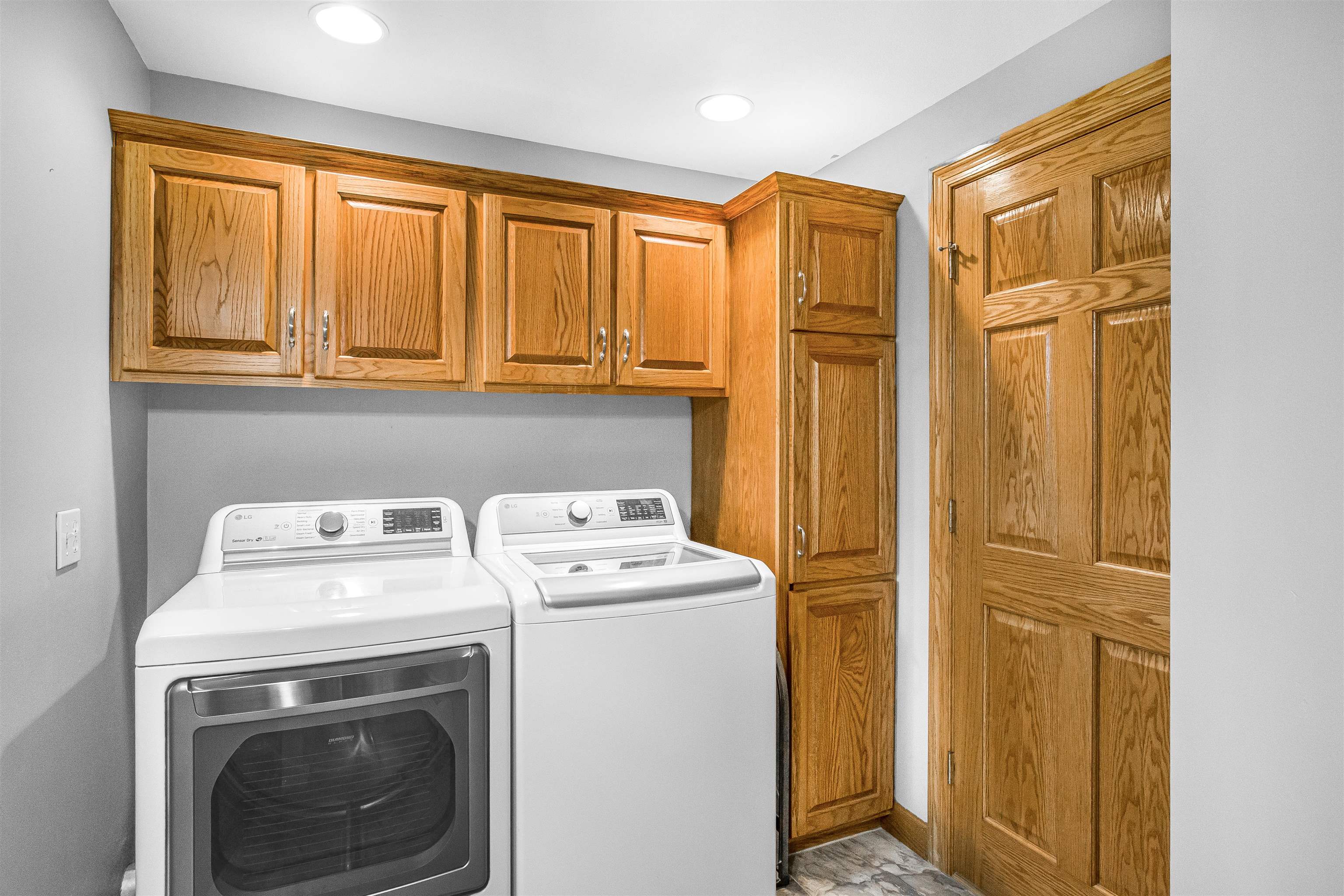 Laundry room with white washer and dryer beneath honey-oak cabinets and beside a matching storage cabinet.