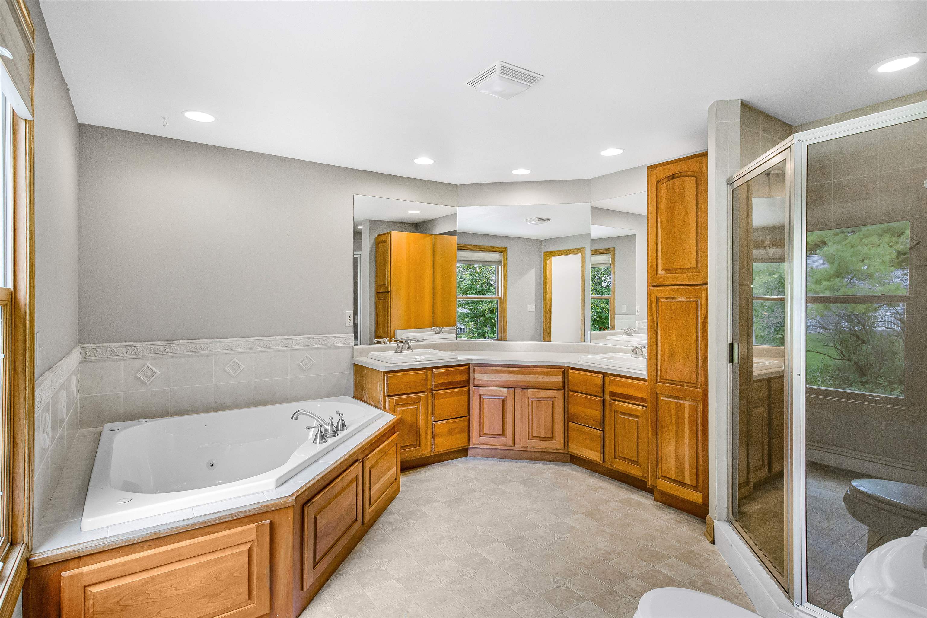 Spacious bathroom with a soaking tub, double-sink vanity, wood cabinetry, and glass-enclosed shower.