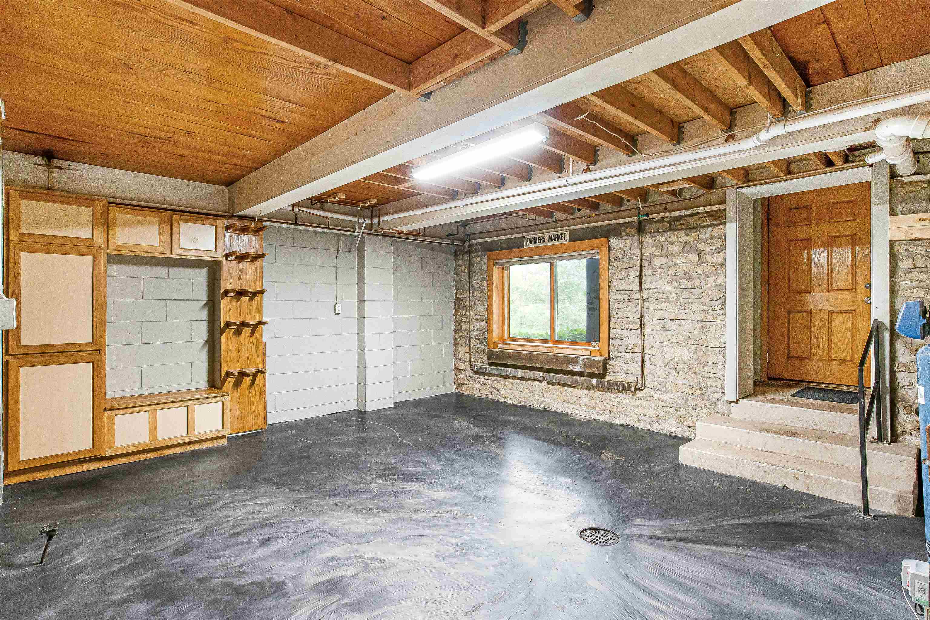 Basement garage with exposed wood ceiling, built-in cabinets, stone wall window, and steps to a wooden door.