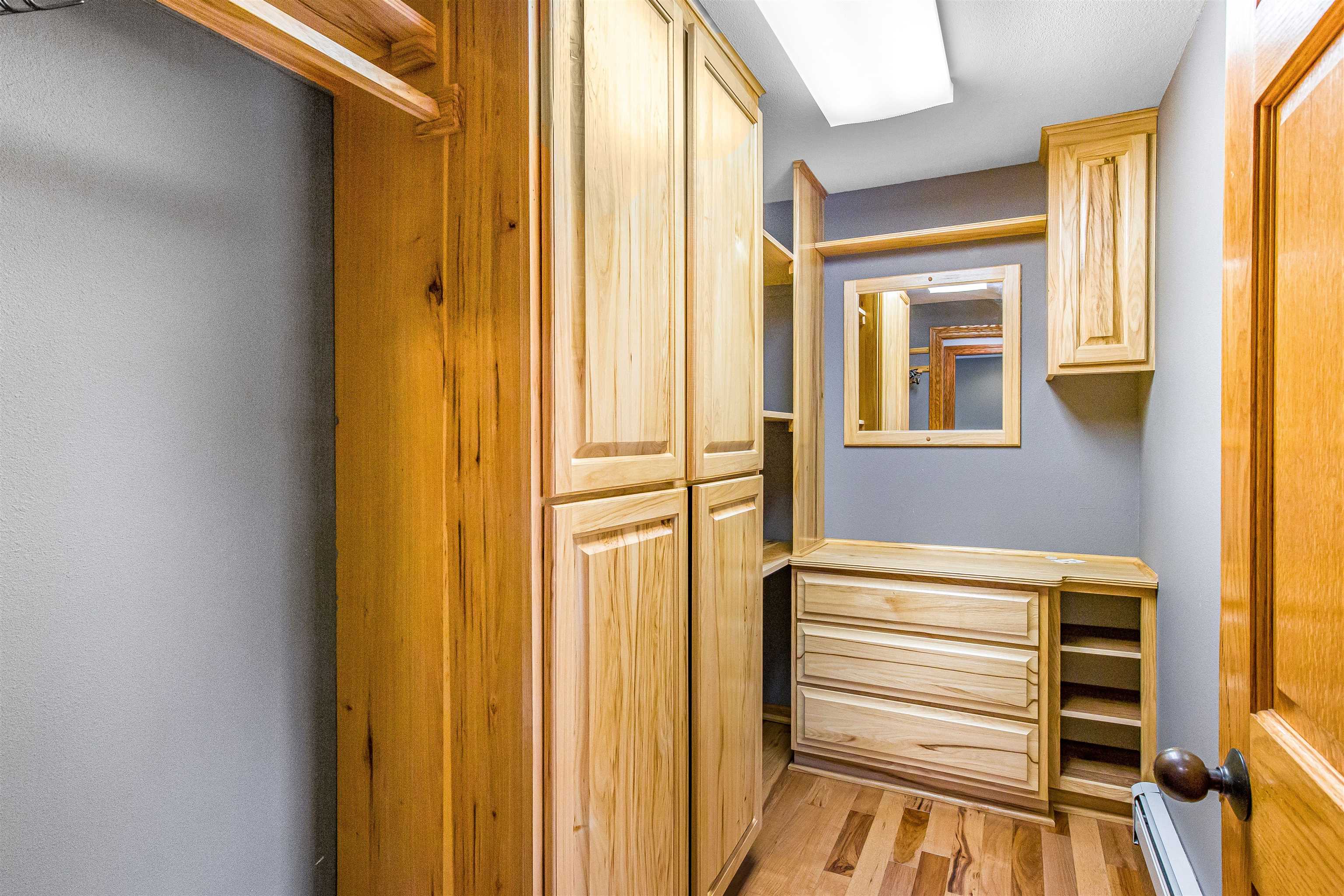 Walk-in closet with light wood built-in cabinetry, a dresser, and a mirror.