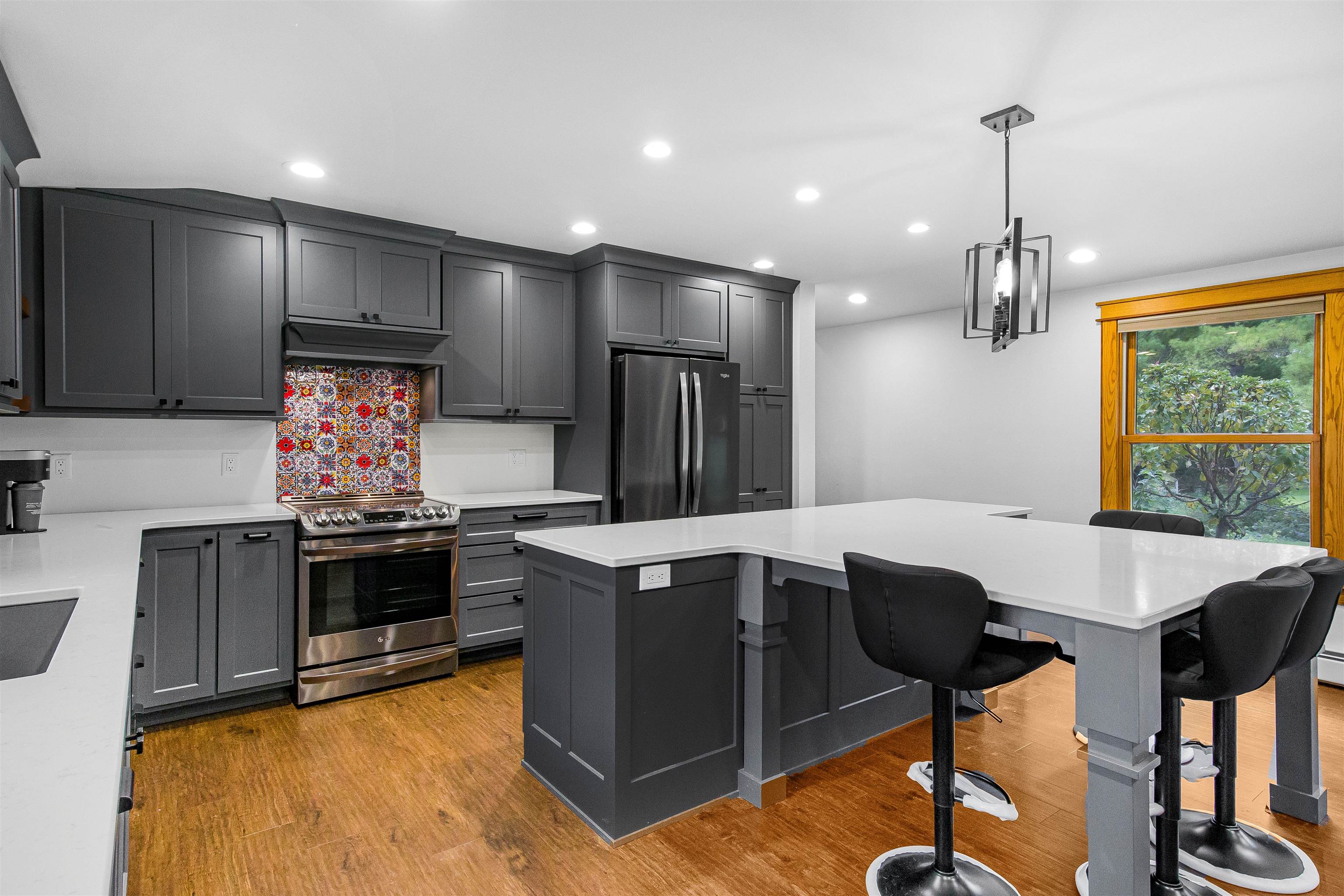 Modern kitchen with dark gray cabinets, a large white island, and a colorful backsplash behind the range.