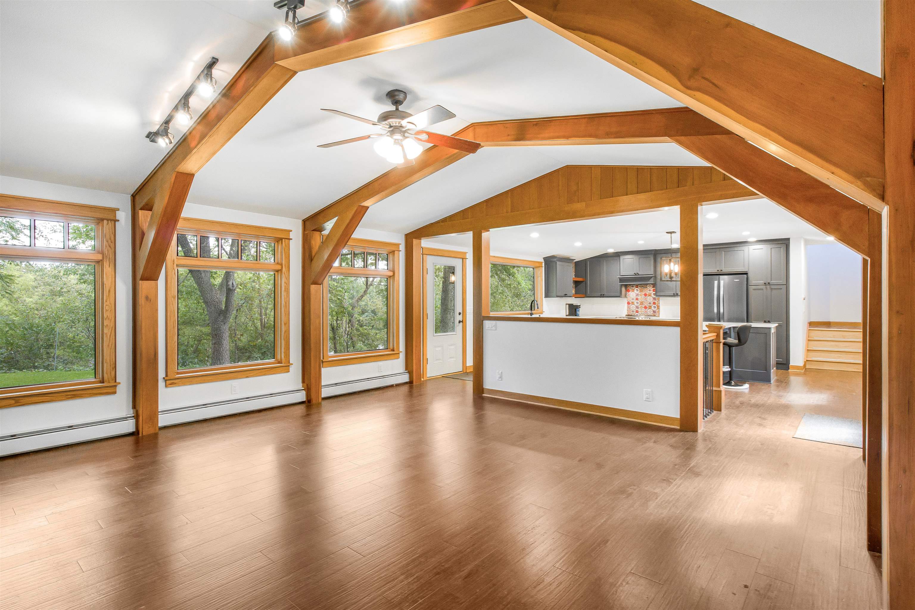 Open living area with exposed timber beams and wood floors, connected to a gray-cabinet kitchen.